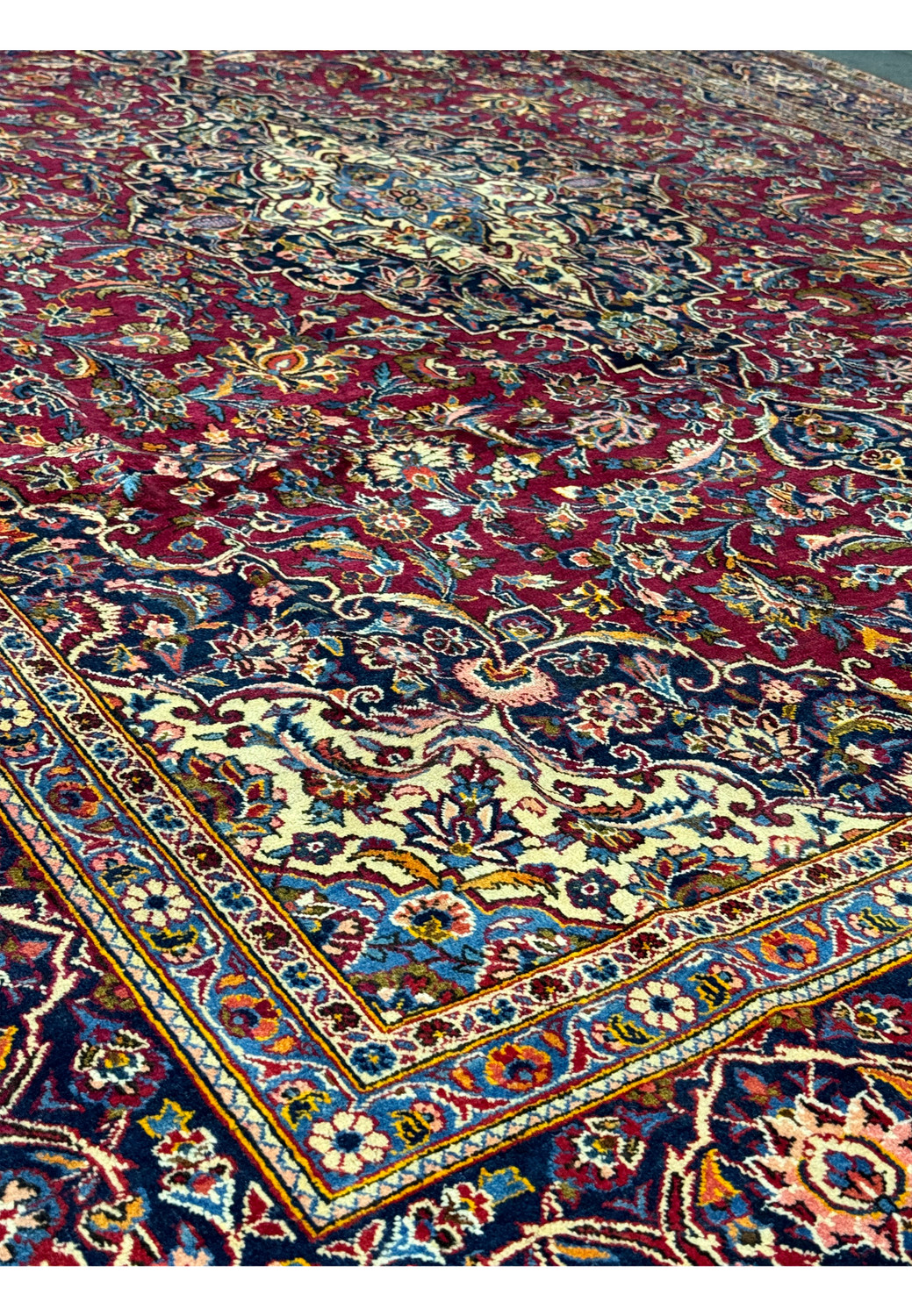 Angled perspective of a Persian Kashan rug with a rich burgundy field and detailed floral patterns with navy and cream borders