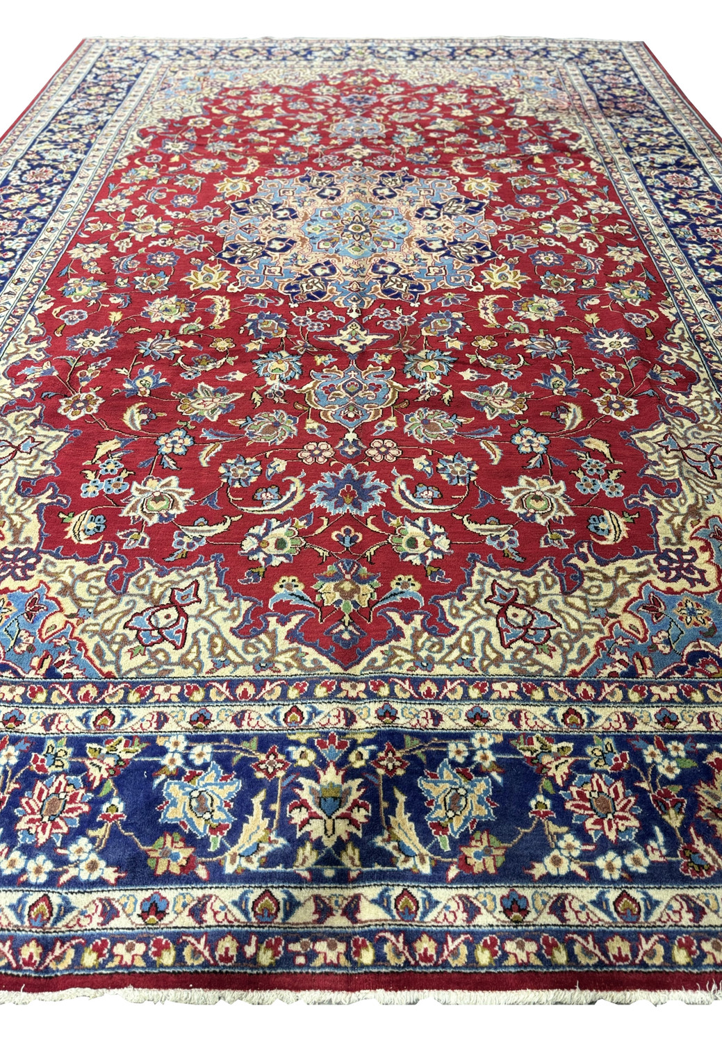 A detailed section of a 10 x 15'6" Persian Isfahan rug, showcasing rich crimson and navy blue with intricate floral and geometric patterns highlighted by cream and indigo accents