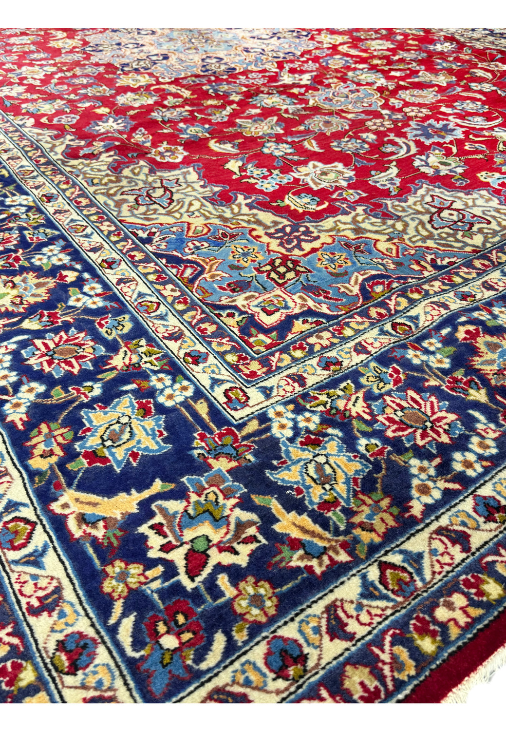 The edge of a rolled 10 x 15 Persian Isfahan rug, highlighting the texture and pattern details with vibrant reds, blues, and creams visible on the layers