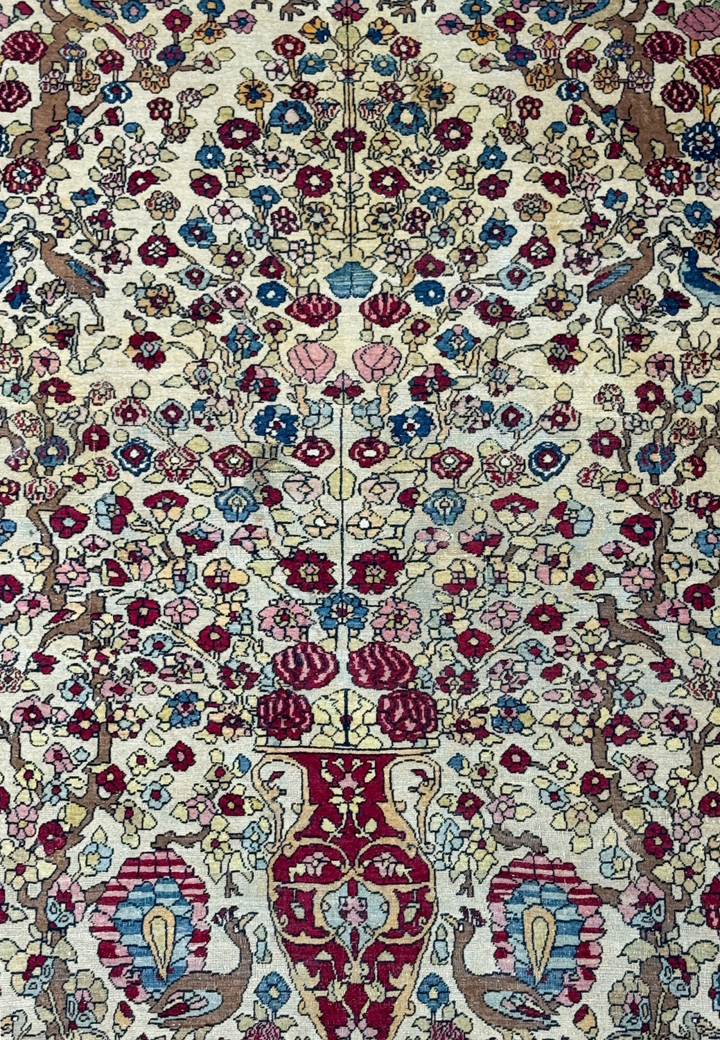 A close-up of the central part of the rug, highlighting the detailed vases and tree of life motif amidst the floral patterns.