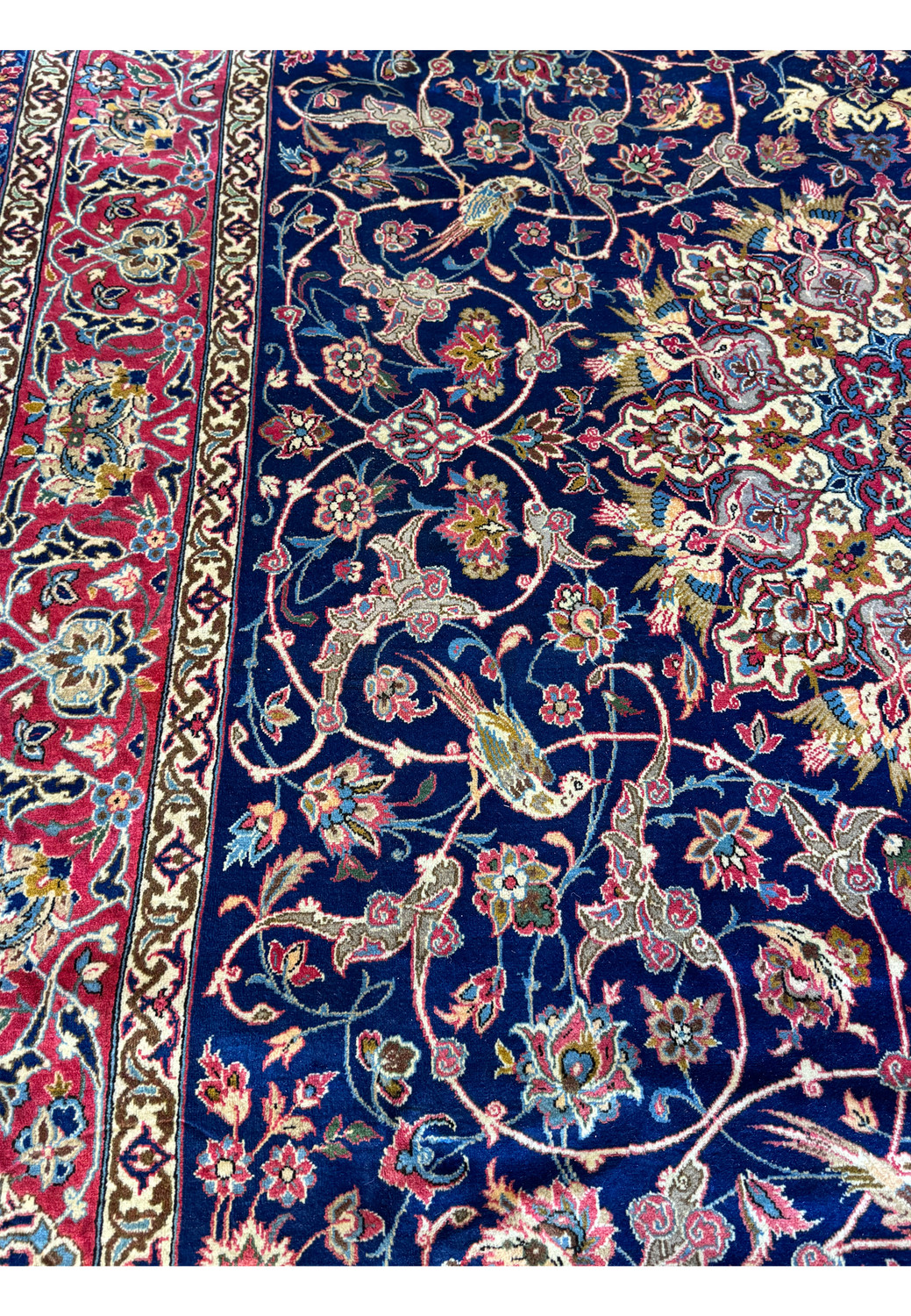 Close-up of a Persian Isfahan rug showing intricate floral designs and bird motifs with a red border.