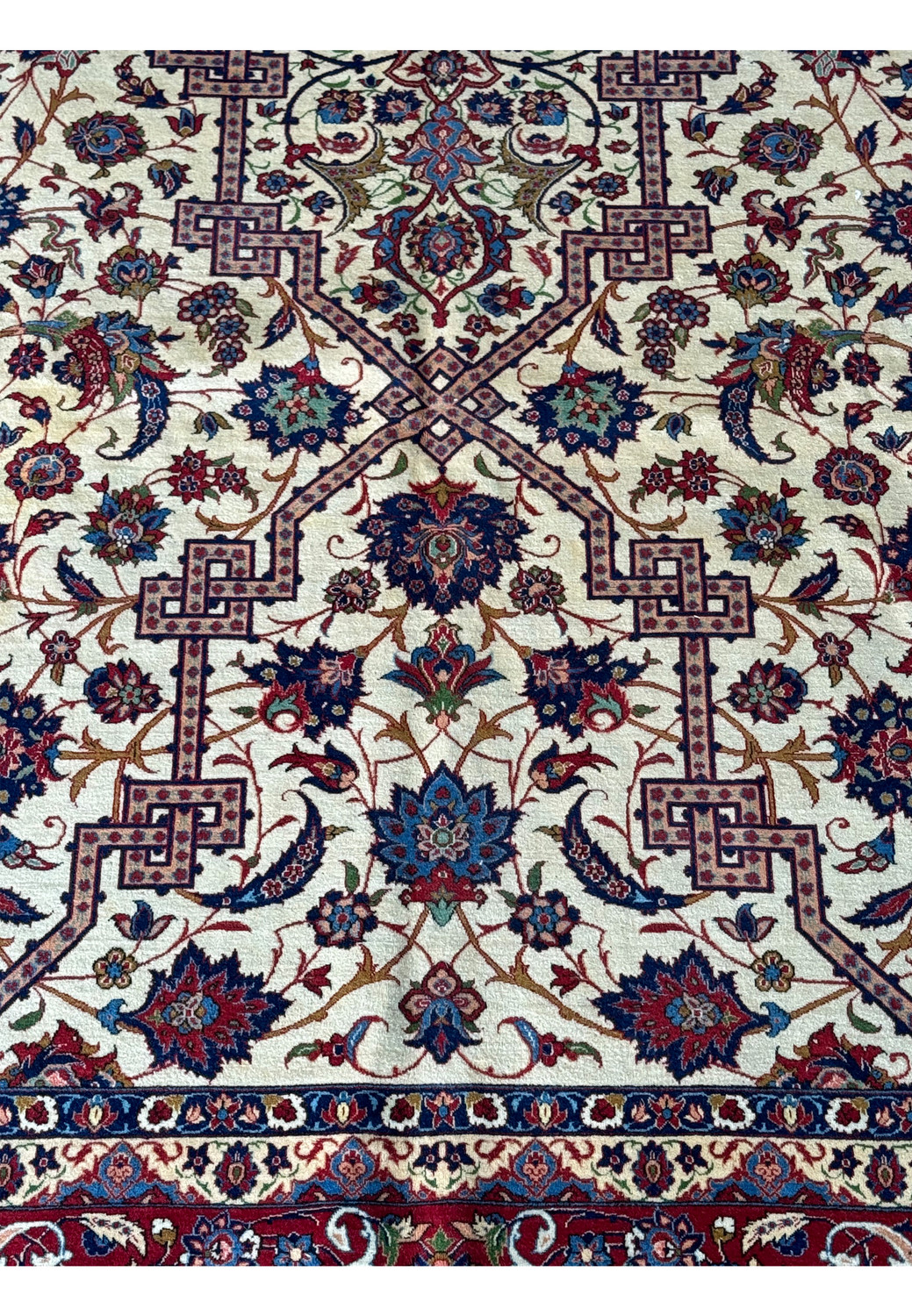 Close view of the Persian Isfahan rug's intricate border patterns with flowers and vines on a red background.