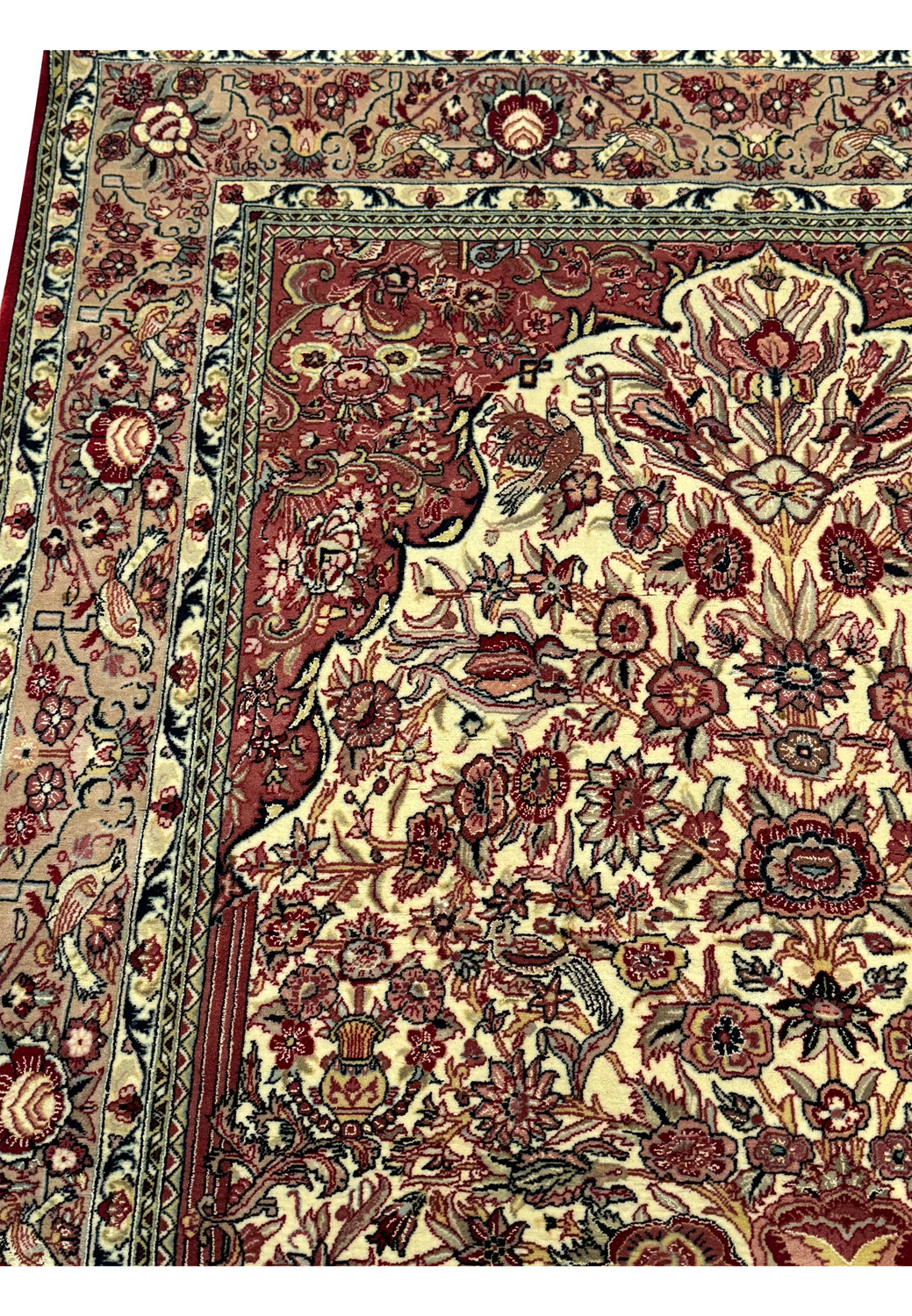 Angled close-up of a Persian Qum rug, highlighting the luxurious wool and silk blend pile, with a detailed view of the border and a section of the central floral medallion motif in a palette of red, cream, and blue.