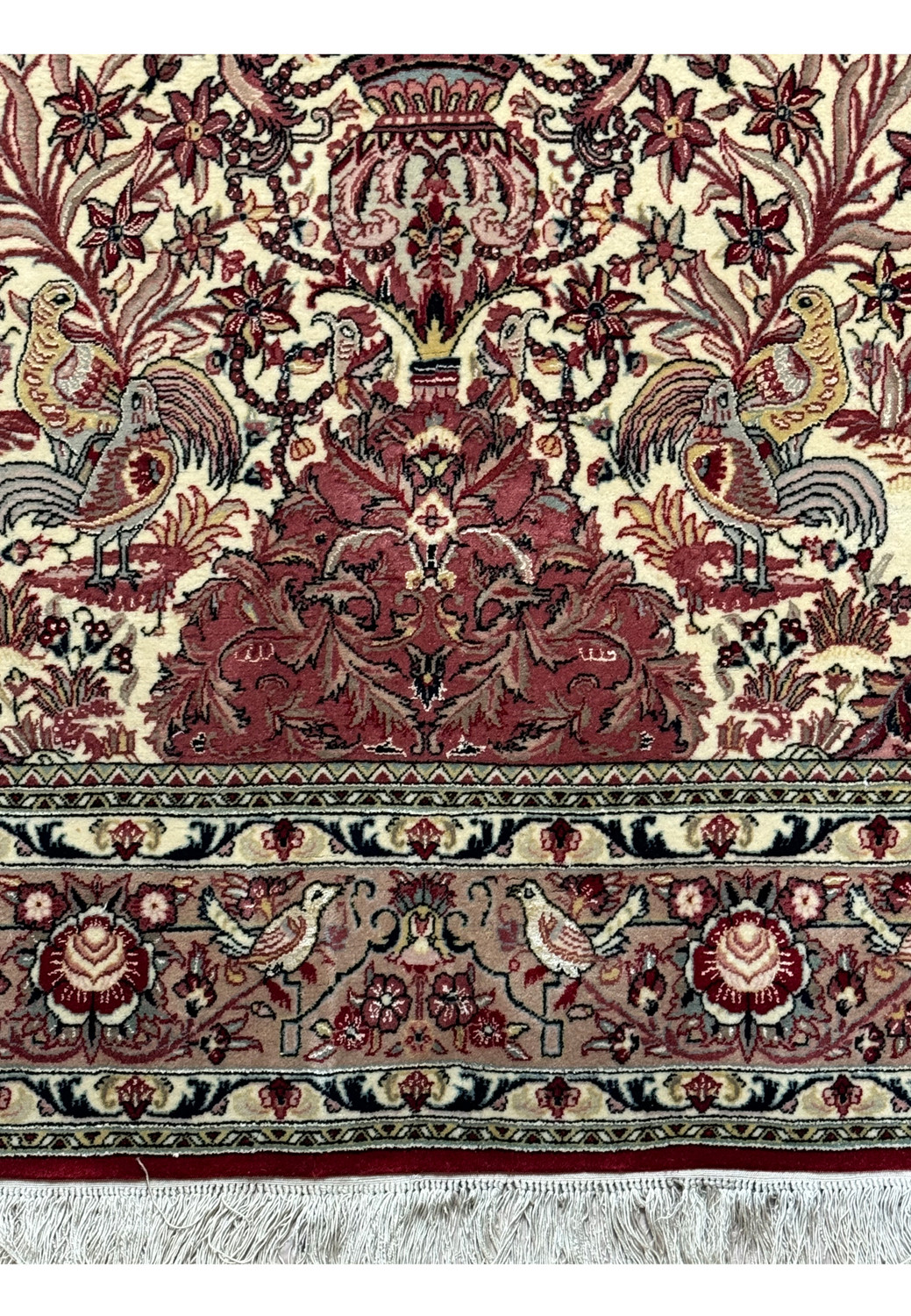 Close-up on the upper half of the Persian Qum rug, showing the detailed floral patterns, bird motifs, and the intricate border that frames the central field.