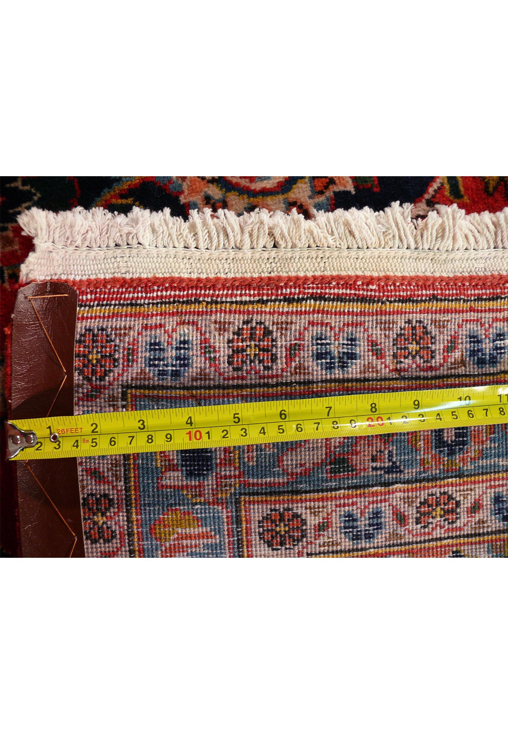 A close-up of the rug's edge with a measuring tape, focusing on the fine weave, the detailed edge patterns