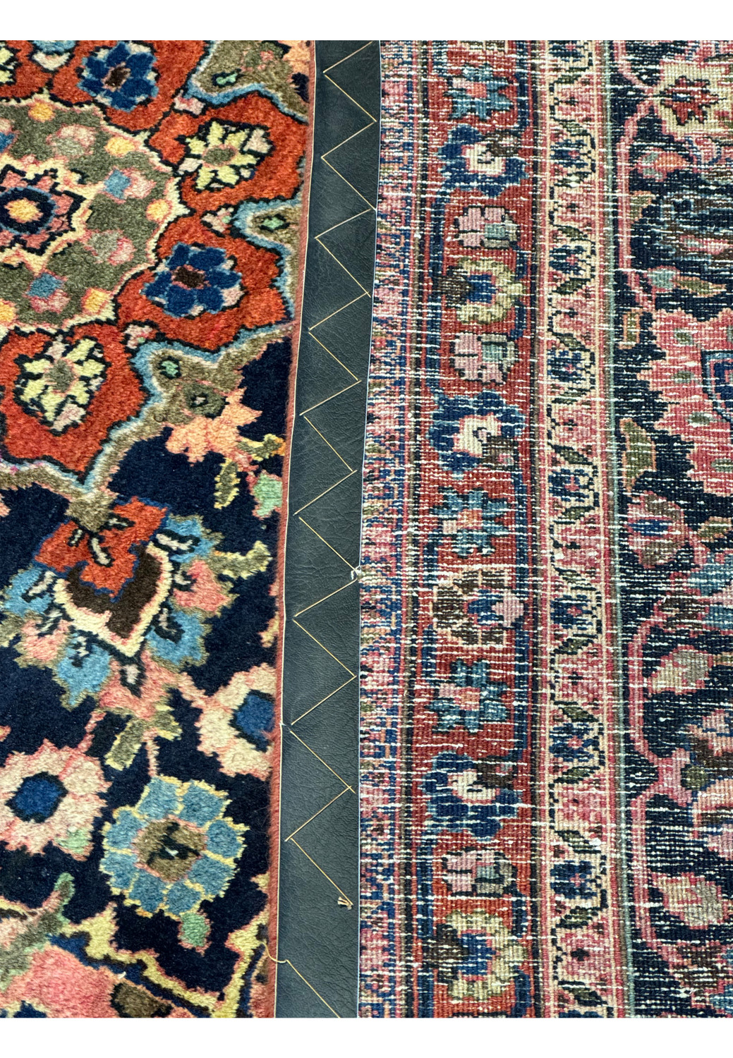 An angled view of a Persian Mashad rug lying against a grey floor, highlighting the contrast between the rug’s elaborate edge patterns, with repeating floral motifs in red, blue, and cream, and the solid, modern floor design, emphasizing the blend of traditional craftsmanship with contemporary styling