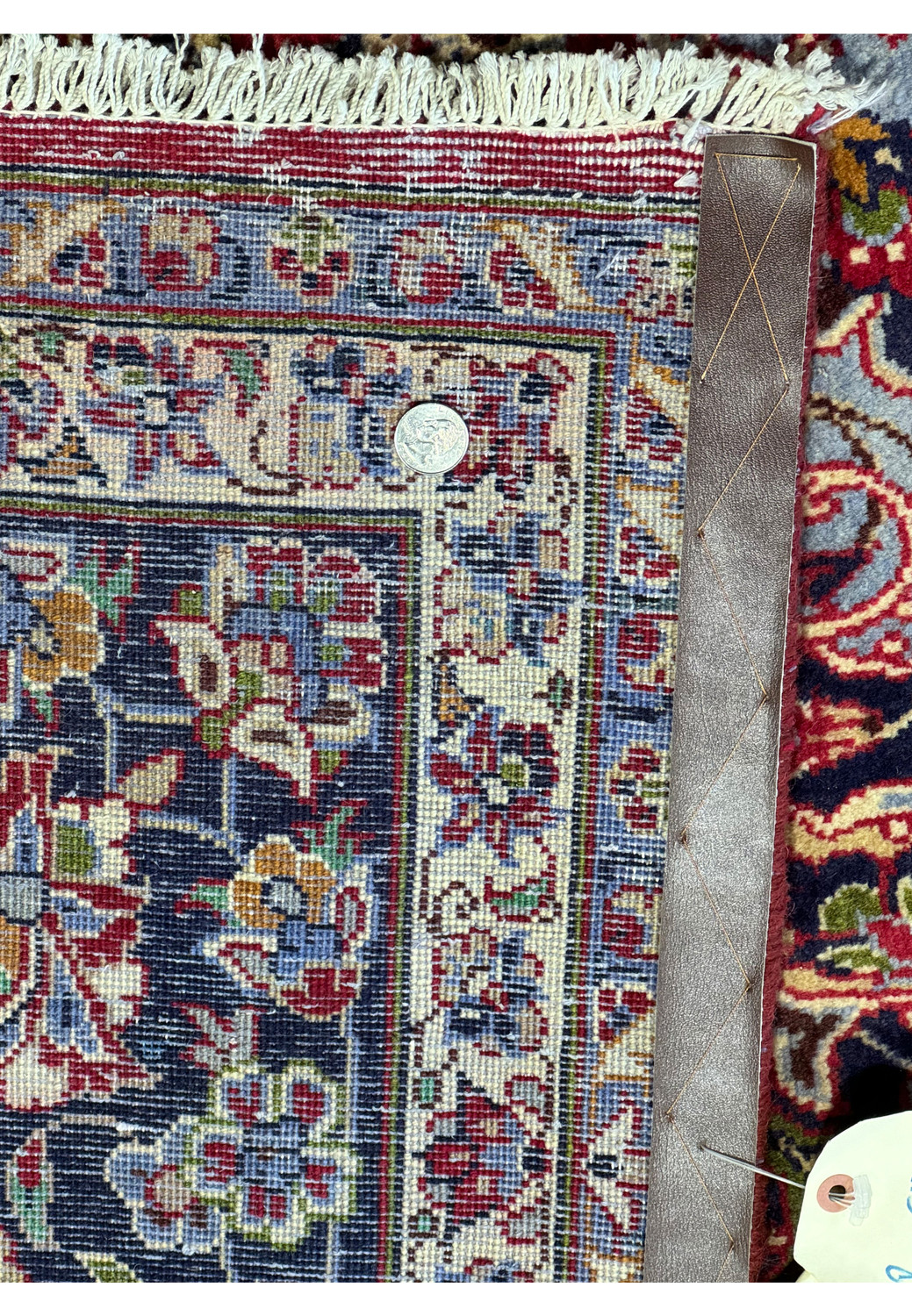 Detailed view of the edge and back of a Persian Isfahan rug with measuring tools - This image displays the edge and back side of the Persian Isfahan rug. A leather runs along the side, illustrating the rug's meticulous craftsmanship and durability. The quarter on the rug serves as a reference for the scale, showcasing the tight, consistent weaving and vibrant coloration that characterize the rug's superior quality.