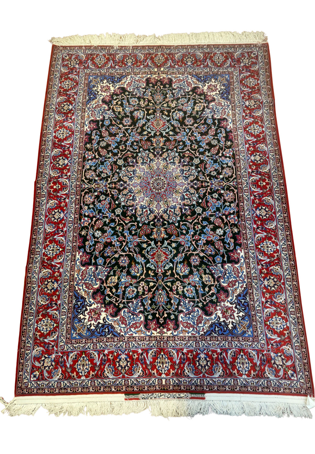 Angled view of signed Persian Isfahan Seirafian rug, hunter green field with central medallion and red floral border.