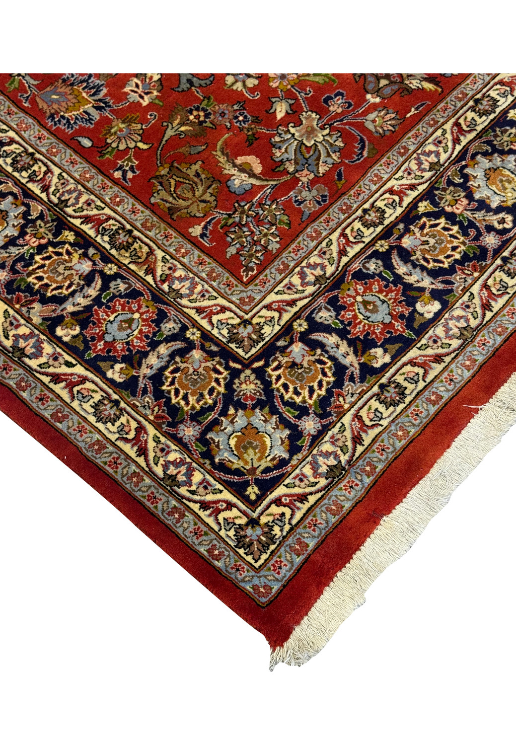 Corner edge of Sarough Persian rug with rust red terracotta field, navy border, ivory guard, and finely knotted fringe on cotton foundation.