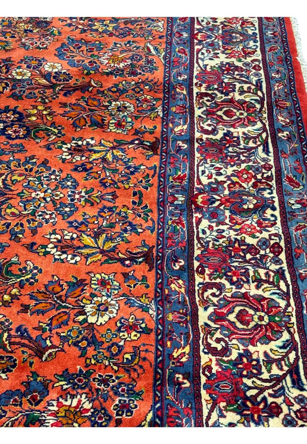Close-up of Persian Sarough rug wool pile, showing coral red base, navy outlines, floral patterns in green, gold, ivory, and burgundy.