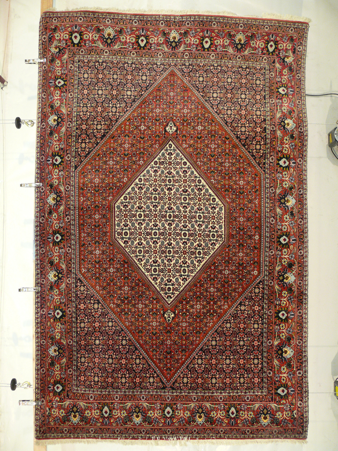 Hanging view of 6'9 x 9'4 Bijar Persian Iron Rug with brick red field, ivory medallion, and floral motifs