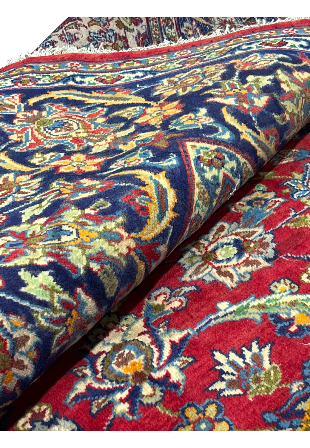 Rolled view of 9'6 x 12 Persian Isfahan rug showing detailed floral patterns in red and navy with fine wool pile and intricate border craftsmanship.