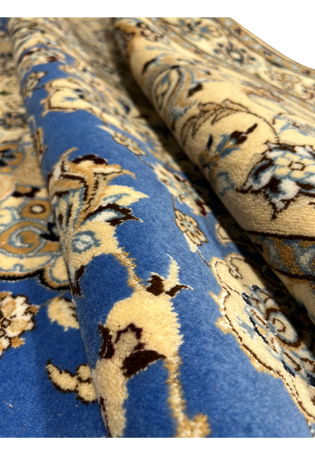 Close-up of rolled Persian Nain 6 LA rug displaying smooth royal blue wool pile, ivory floral vines, and fine beige silk outlines in delicate craftsmanship.
