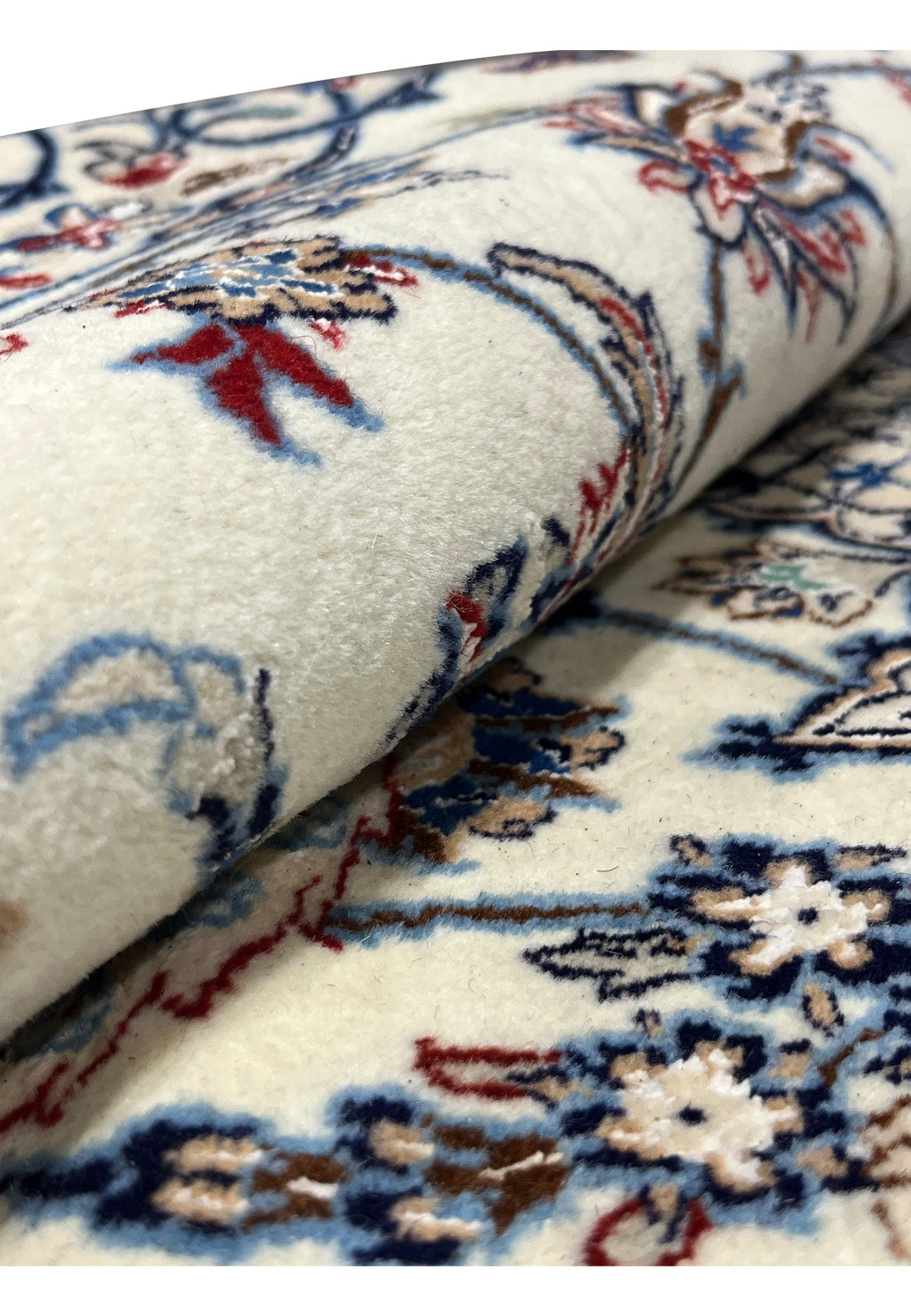 Rolled section of Persian Nain 4 LA Habibian rug highlighting its ivory wool pile, fine silk sheen, and detailed floral motifs in red, blue, and beige.