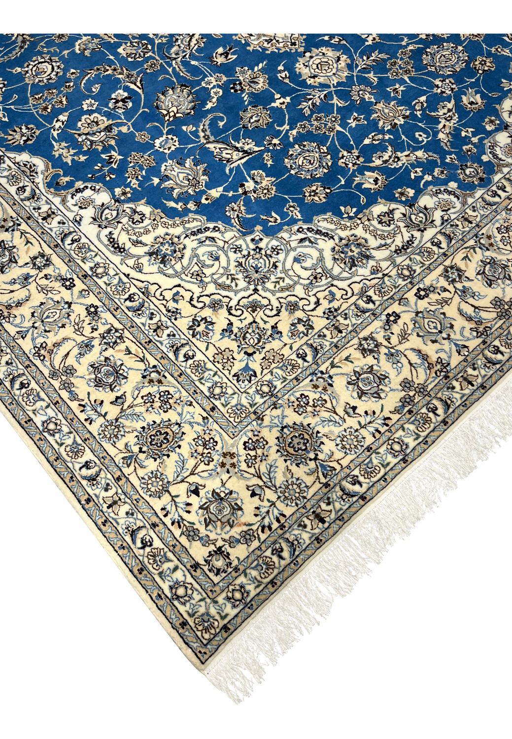 Angled corner view of royal blue Persian Nain rug with ivory floral border and white fringe.