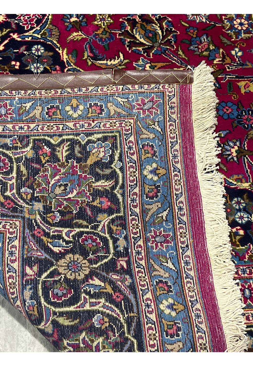 Close-up of the backside of Mashad rug corner showing cotton fringe, blue guard border, and precise hand-knotted details.
