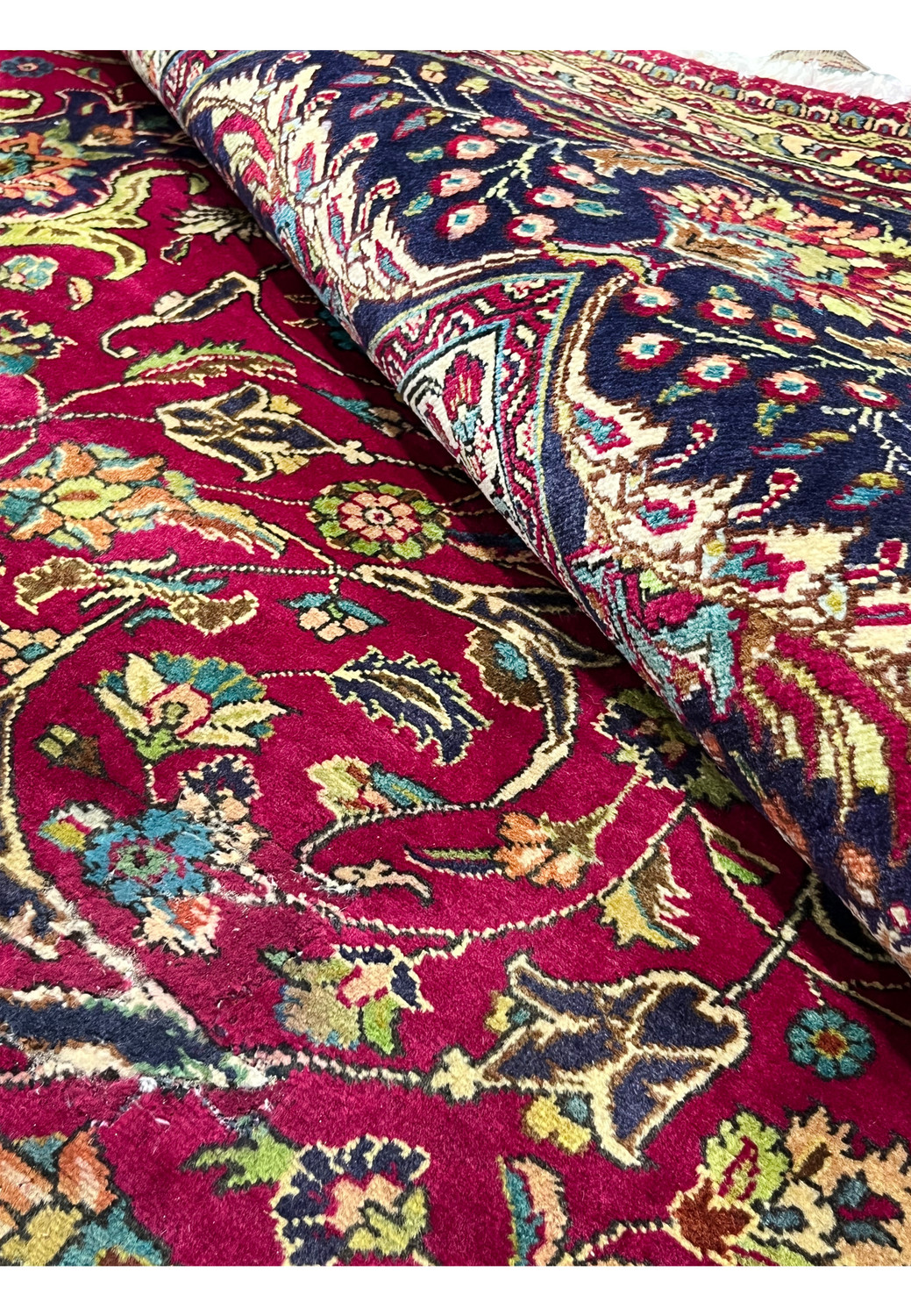 Close-up folded view of the vintage Persian Tabriz rug revealing the red field, floral patterns, and plush wool pile texture on a cotton foundation.