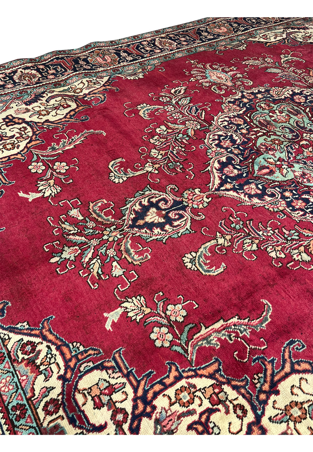 Macro closeup of vintage Persian Tabriz rug showing worn pile, patina, and fine floral outlines against the distressed red field.