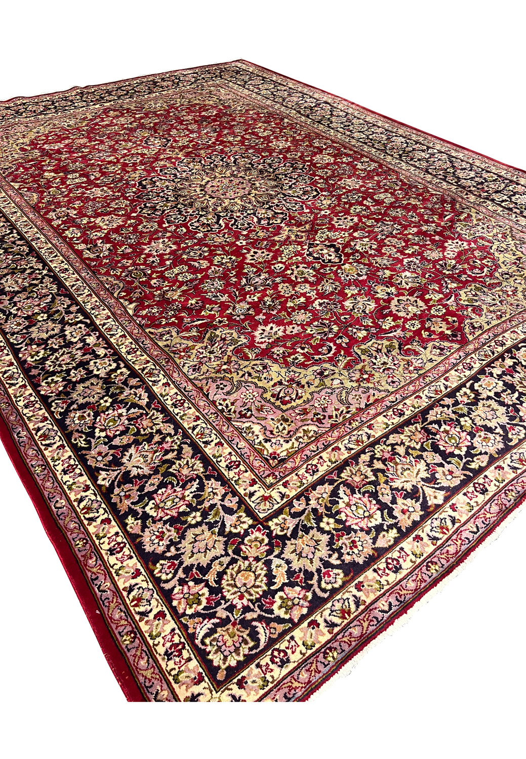 Angled view of large red Persian Isfahan rug showing navy floral border and medallion