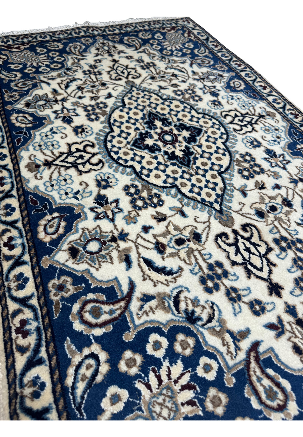 Angled view of Persian Nain rug highlighting royal navy blue field, ivory floral medallion, powder blue accents, and fine wool texture
