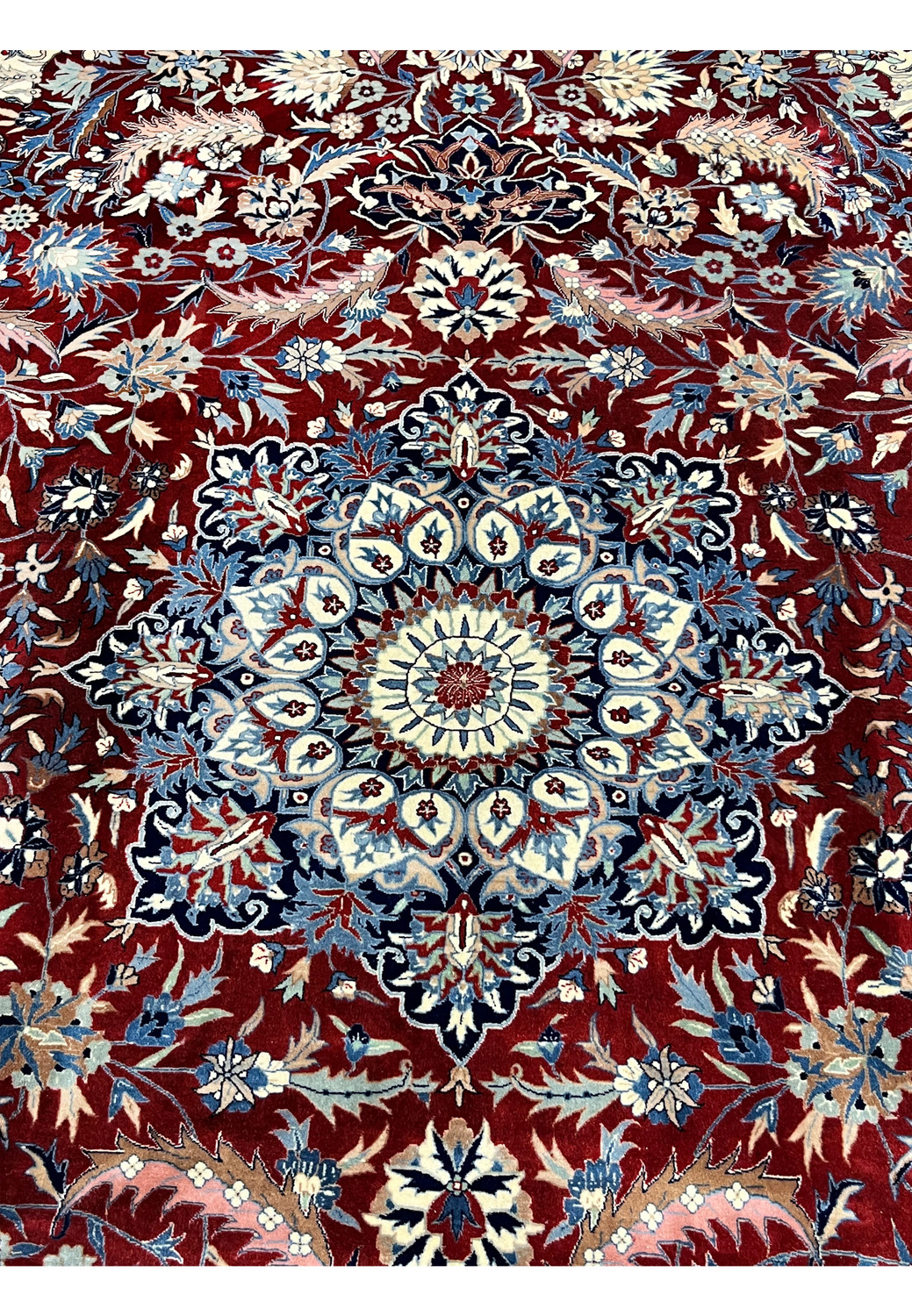 Central medallion of Persian Isfahan rug with layered floral rosettes, ivory and light blue highlights on a deep red background
