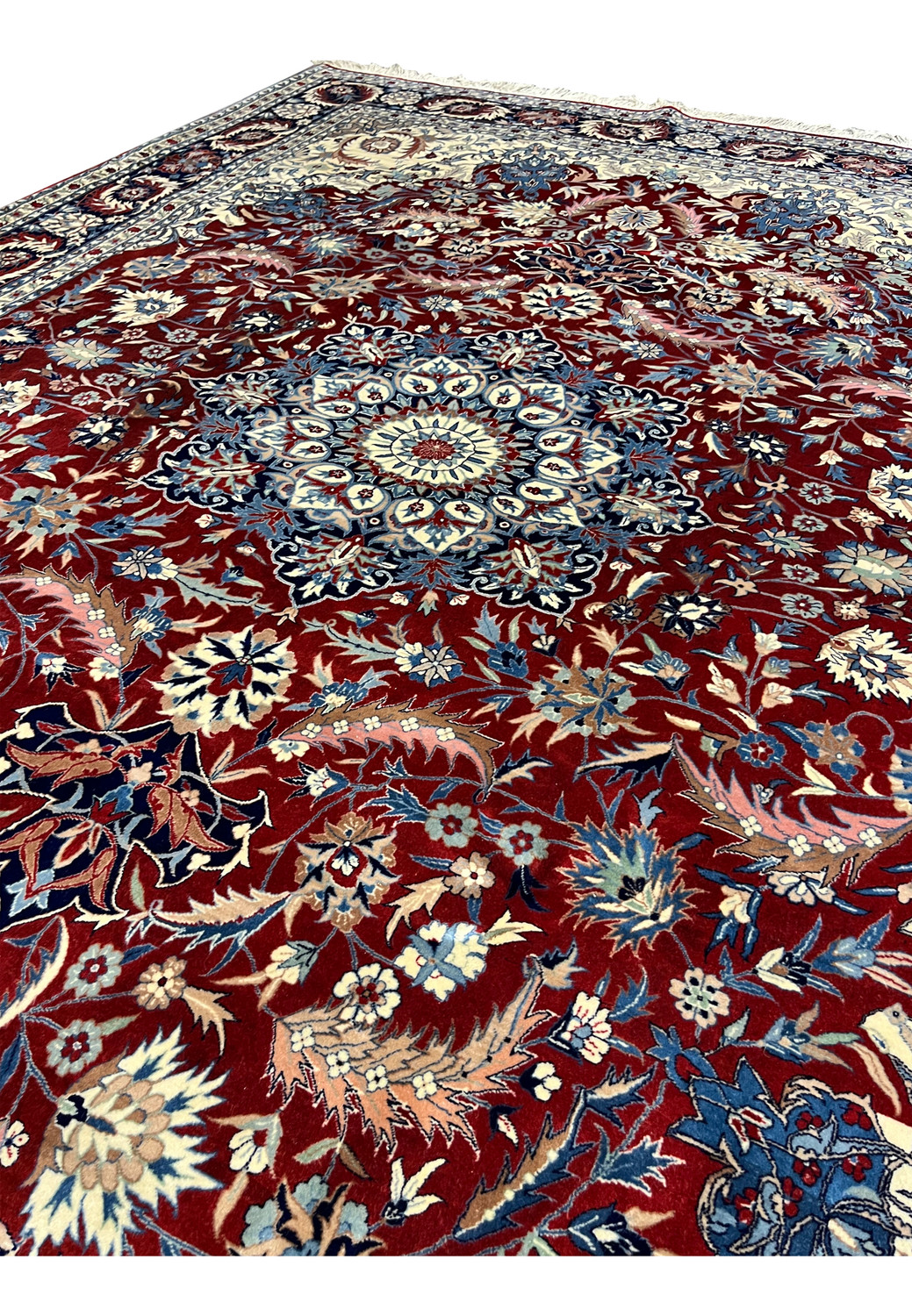 Angled view of Persian Isfahan rug highlighting red floral field, layered blossoms, scrolling vines, and central medallion depth.