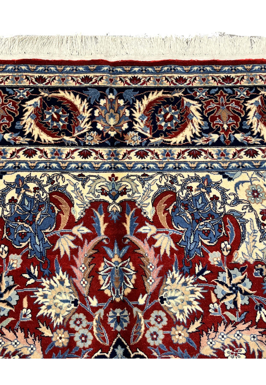 Upper end border detail of Persian Tabriz rug with navy floral border band, ivory accents, and fringe at the top