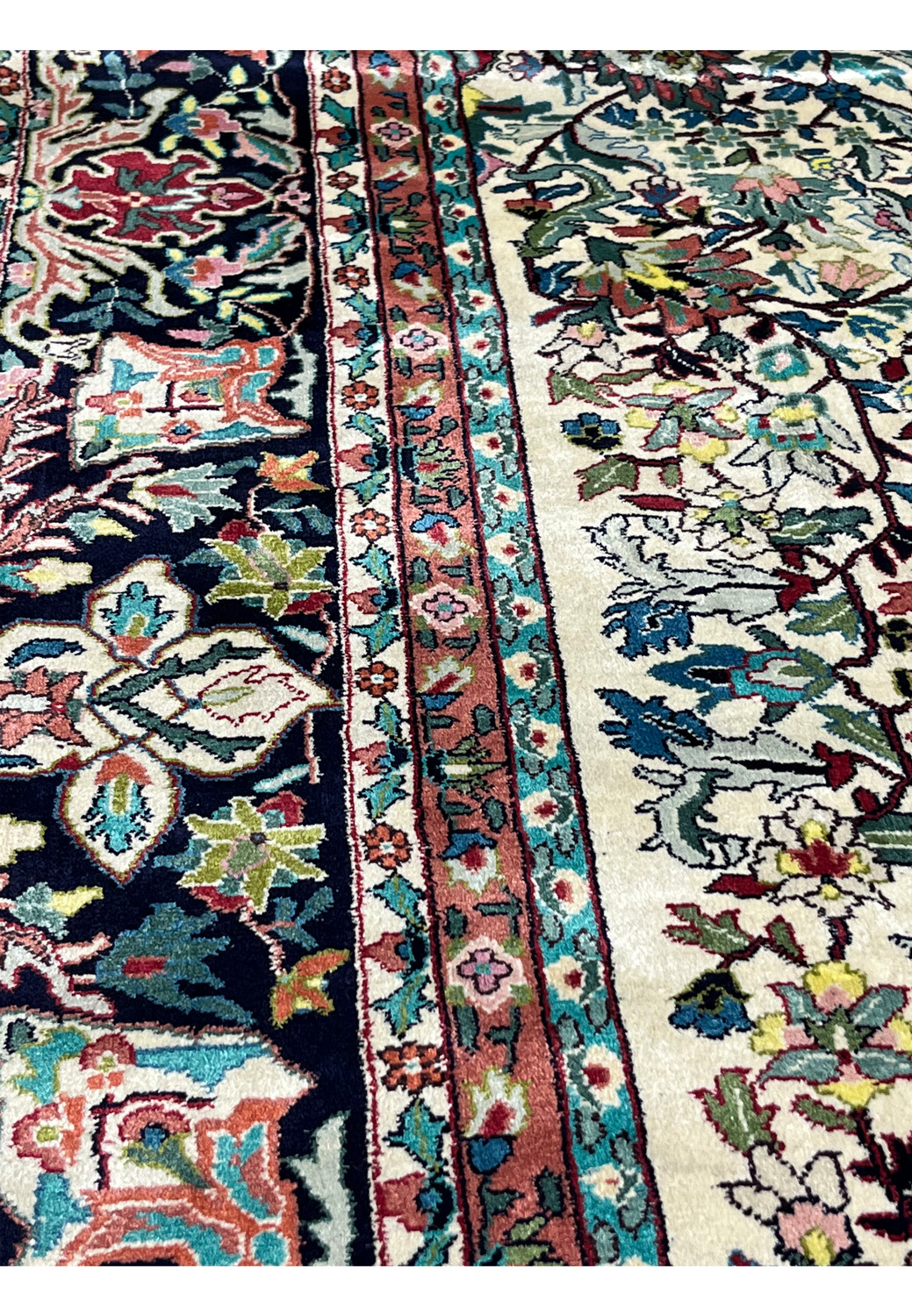 Color detail close-up of silk rug fibers displaying rich contrast between ivory background and saturated reds, blues, and greens