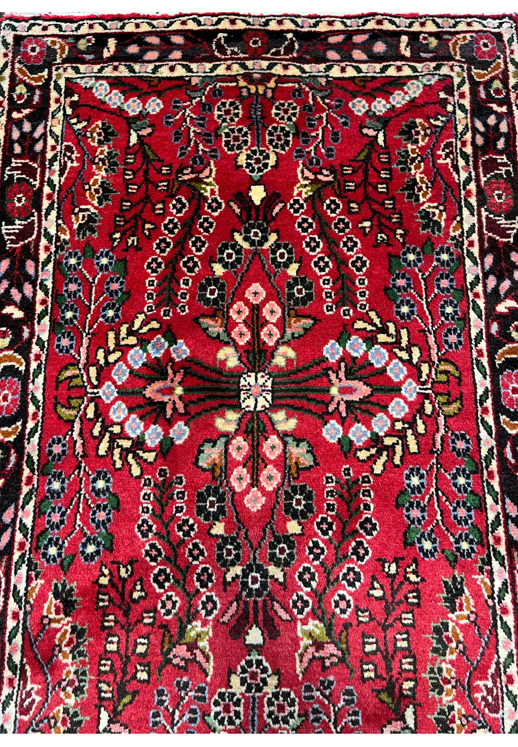 Midfield close-up of a Persian Darjazin rug showing a detailed floral medallion, layered blossoms, vine scrolls, and precise knotting within a deep crimson ground