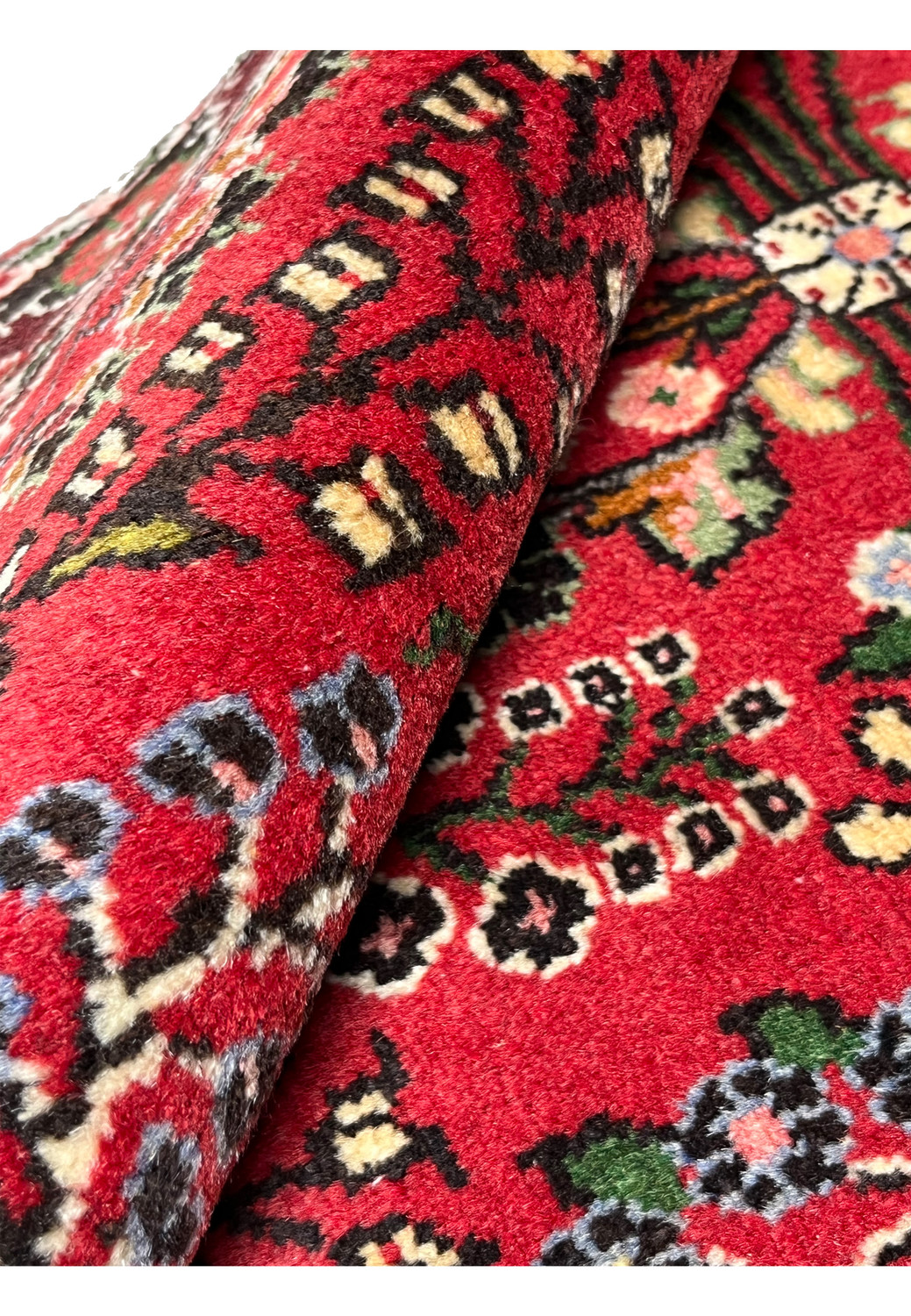 Rolled view of a Persian Darjazin rug revealing dense wool pile, compact hand-knotting, strong structure, and saturated crimson coloration