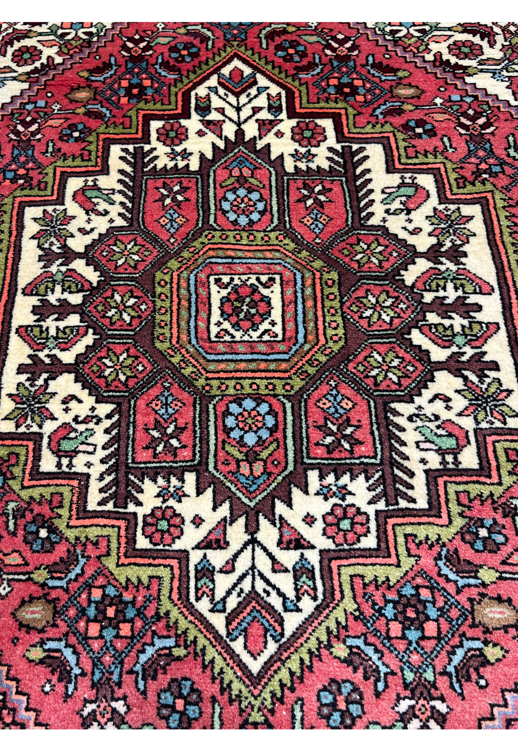 Close-up of geometric medallion on Persian Gholtogh rug with ivory, coral, olive green, and sky blue details