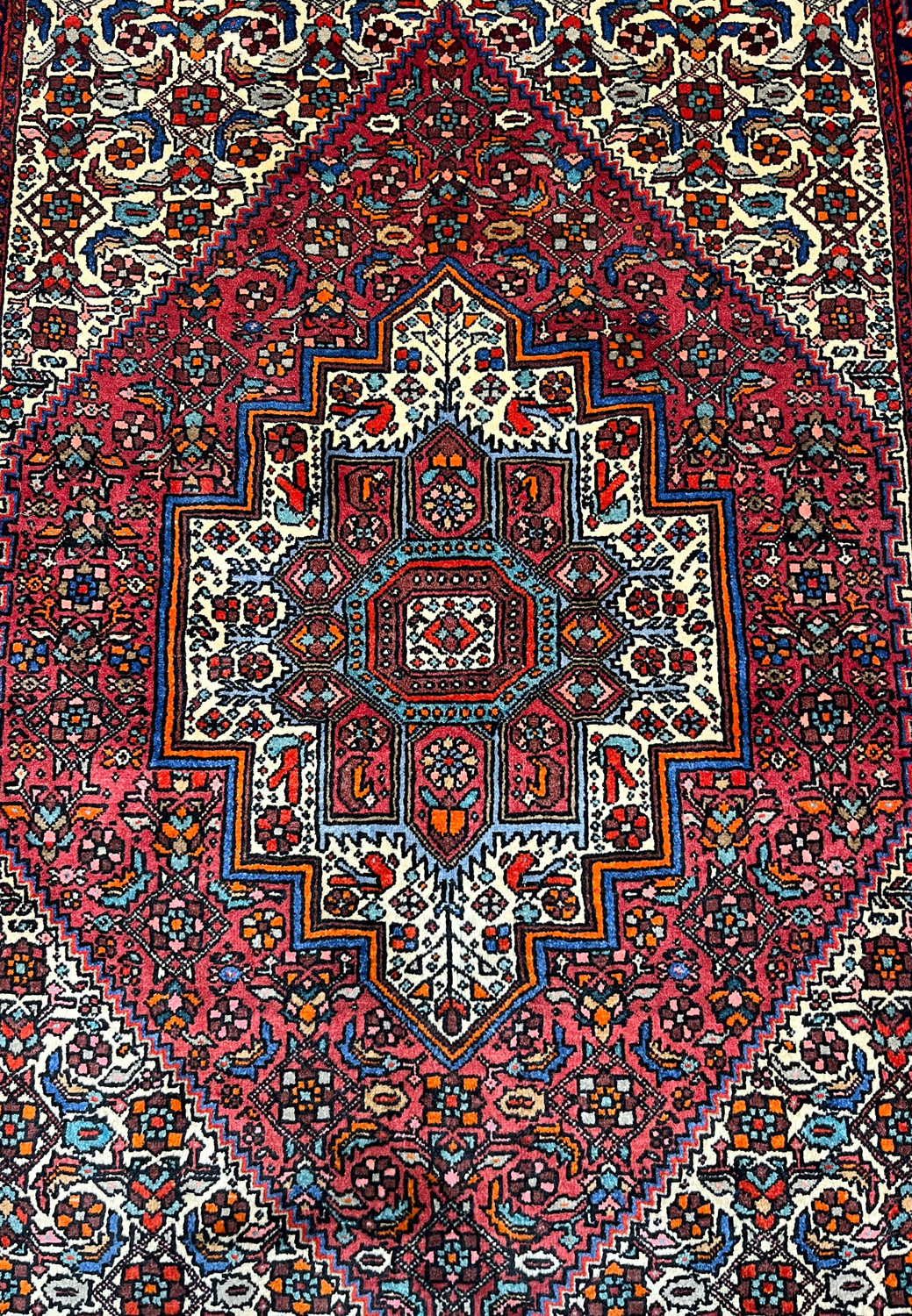 Close-up of the central geometric medallion in a Persian Gholtogh rug, highlighting precise knotting, stepped outlines, rich red tones, and ivory contrast