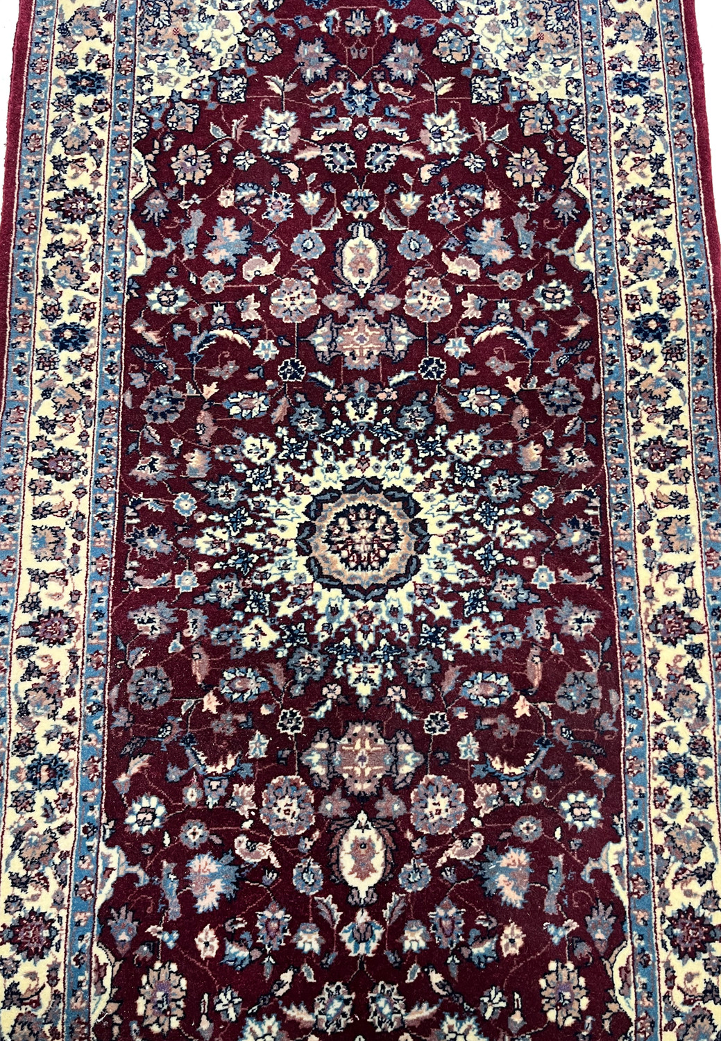 Close view of the central medallion on a Persian Tabriz rug showing ivory and navy detailing, fine knotting, and dense floral symmetry on a burgundy field.