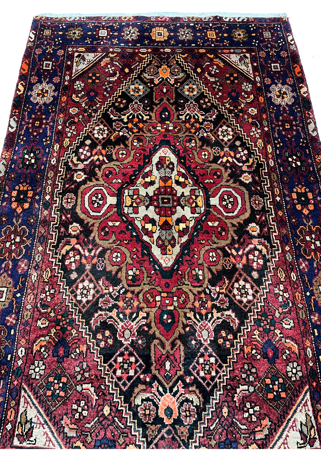 Midfield detail of a Persian Gholtogh rug highlighting layered tribal motifs, saturated red tones, black outlines, and dense wool pile