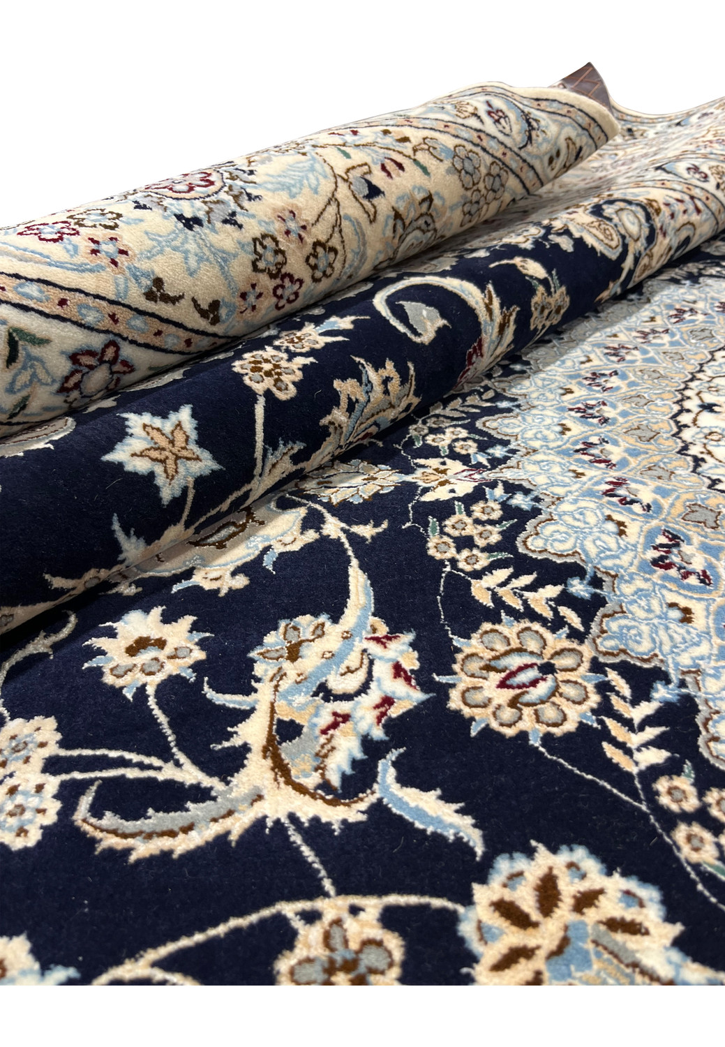 Rolled view of a handmade Persian Nain 6LA rug showing thickness, flexibility, and contrasting navy field against ivory border while partially rolled
