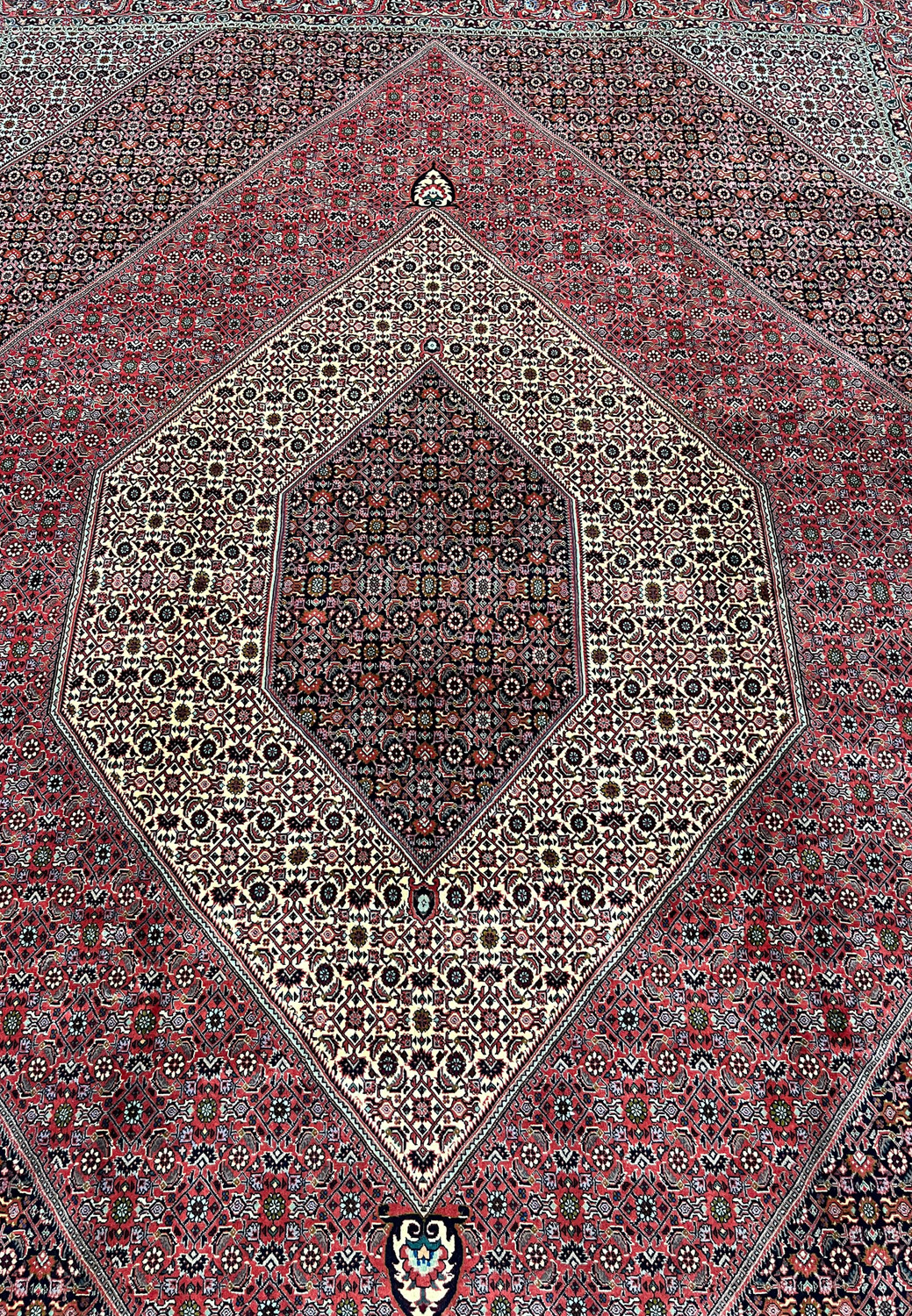 Central field detail of a Persian Bijar iron rug showing dense geometric elements, tight knotting, ivory accents, and rich brick red background
