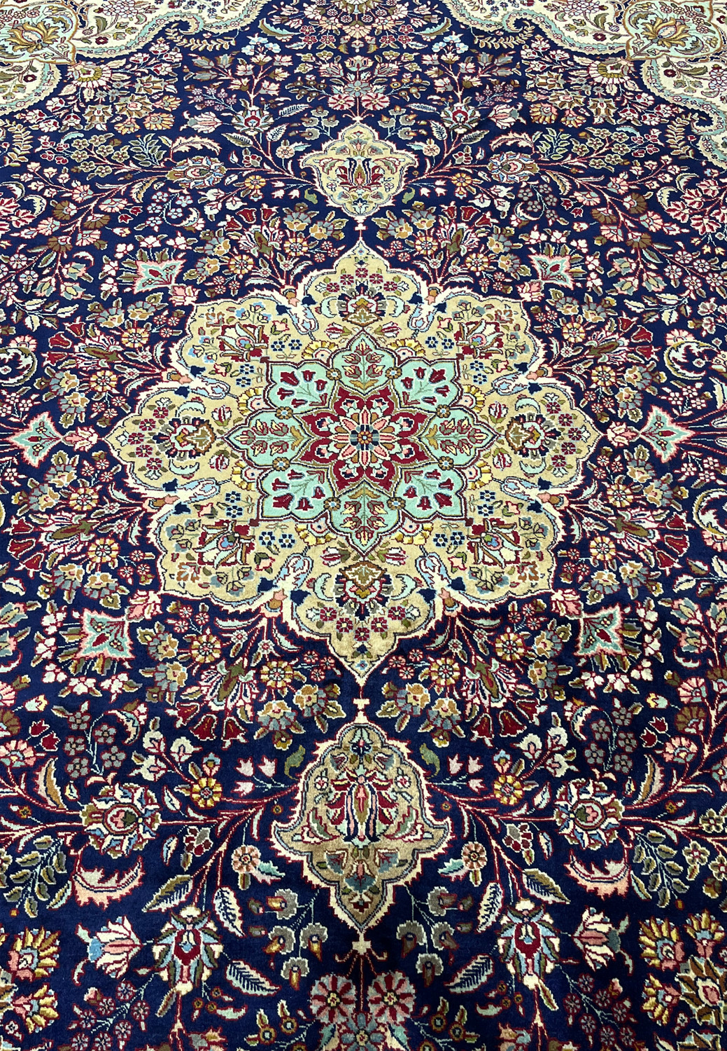 Central medallion of Persian Tabriz rug with ivory, light blue, burgundy, and gold tones set on a deep navy background