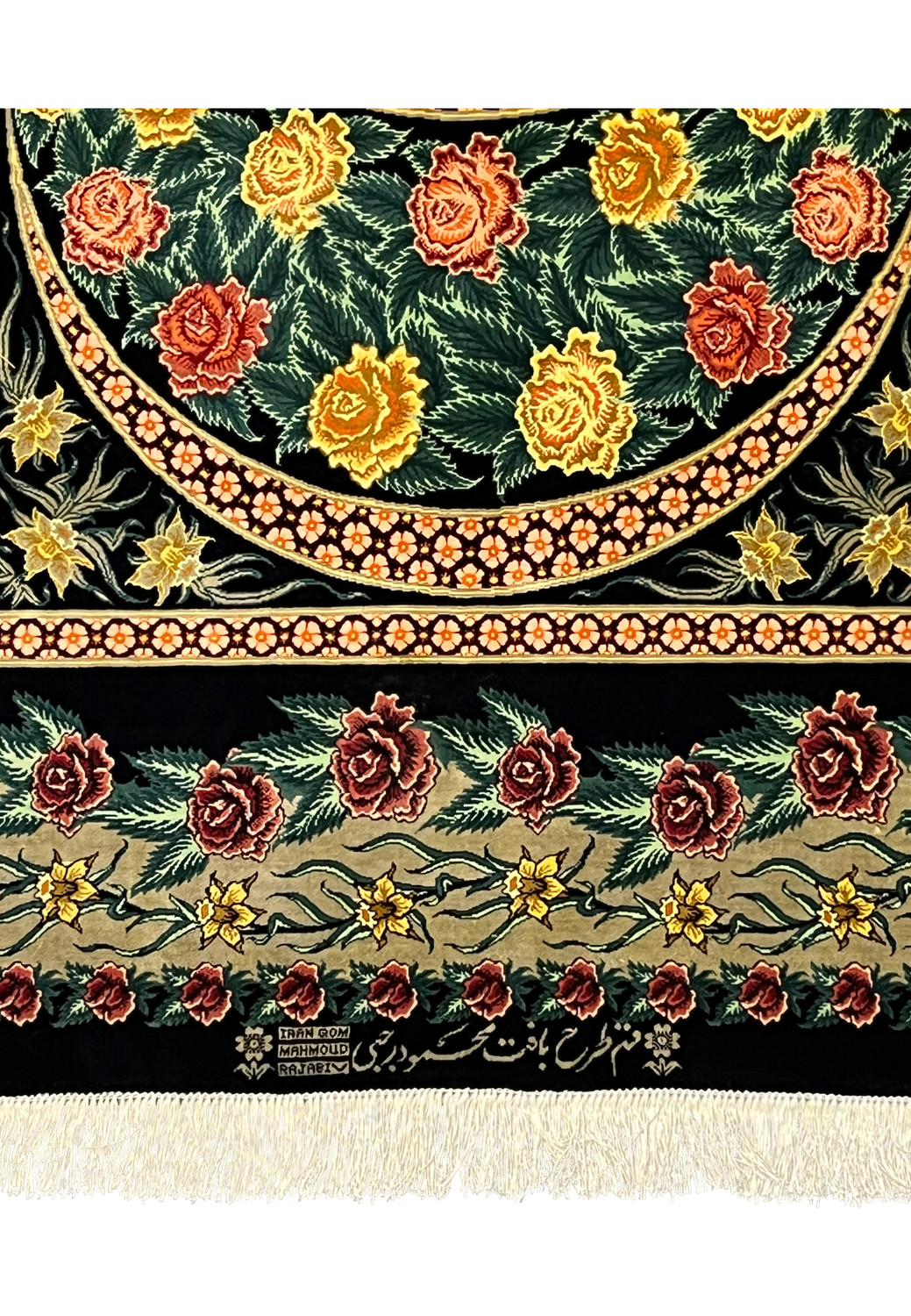 Woven signature detail on a Persian Qum pure silk rug reading Mahmoud Rajabi, placed above the fringe and framed by floral motifs and Iranian origin marks