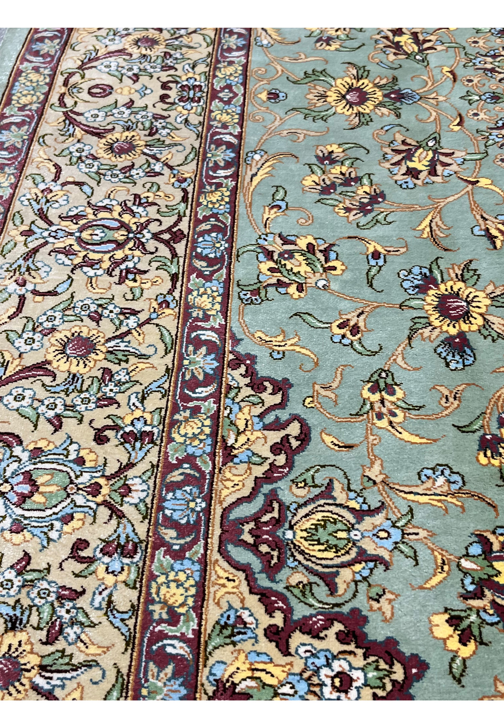 Angled side view of Persian Qum pure silk rug highlighting silky texture, tight knot structure, sage green field, and scrolling floral design