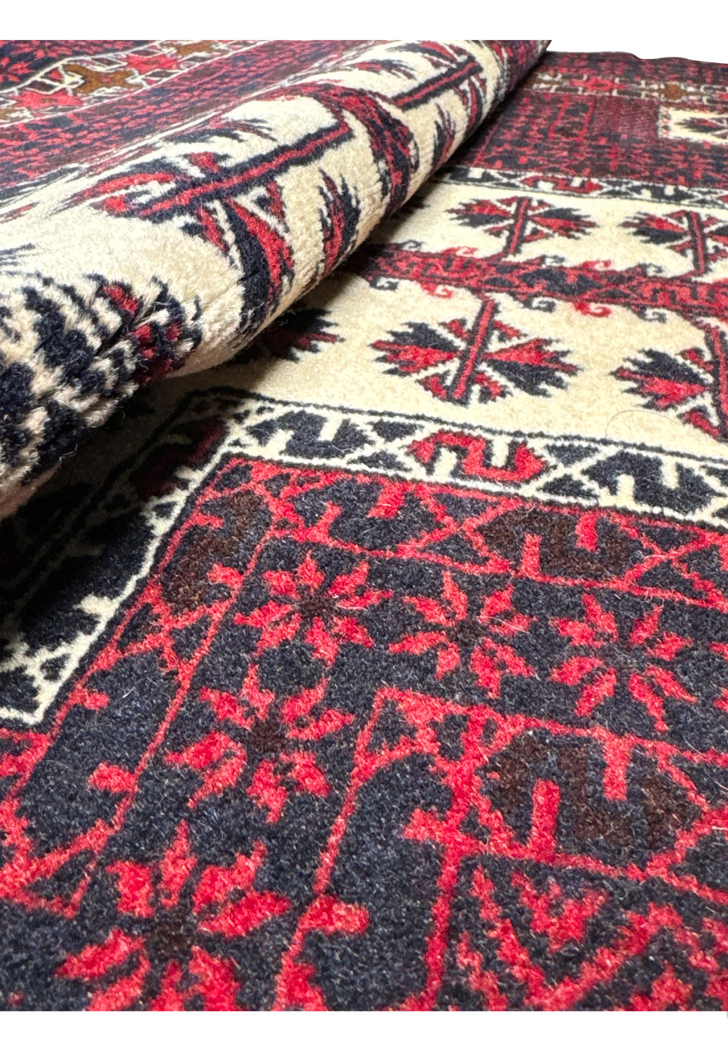 Rolled view of a Persian Baluch prayer rug showing flexible wool pile, rich burgundy color, and compact hand-knotted construction