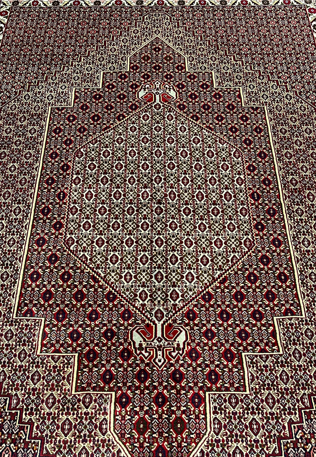 Central medallion detail of Persian Senneh rug with stepped diamond geometry, ivory framing, and dense burgundy and brown pattern fill.
