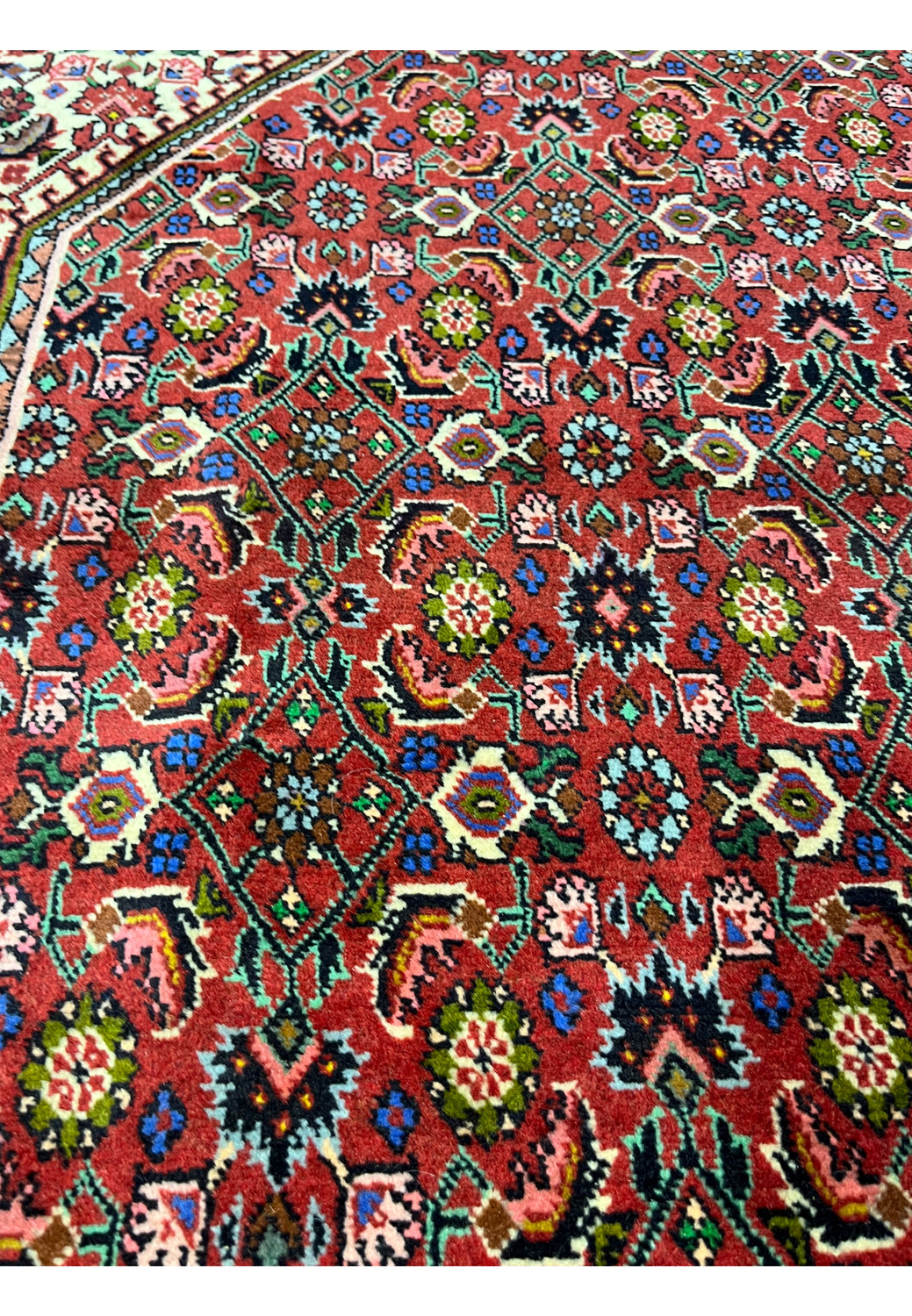 Color detail of Persian Bijar rug displaying brick red, ivory, olive green, soft blue, charcoal black, and beige accents in dense geometric layout