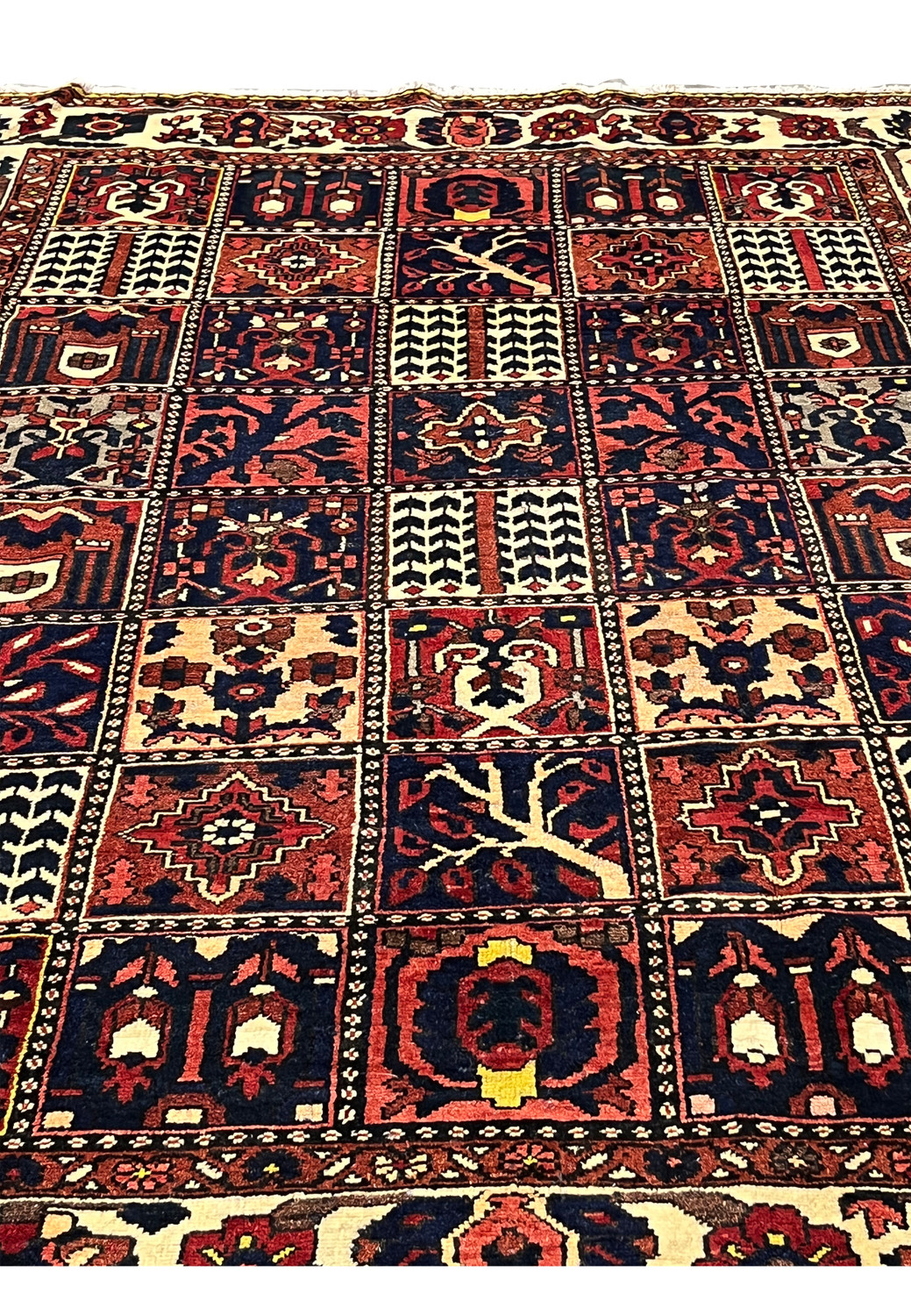 Midfield detail of a Persian Bakhtiar garden pattern rug highlighting pictorial square panels with tree motifs, floral symbols, navy blue grounds, and red accents