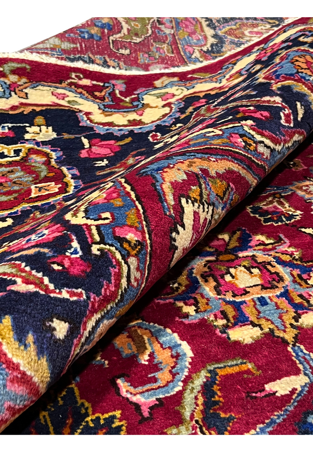 Rolled view of Persian Mashad rug showing thickness, flexible wool pile, saturated colors, and well-preserved structure.