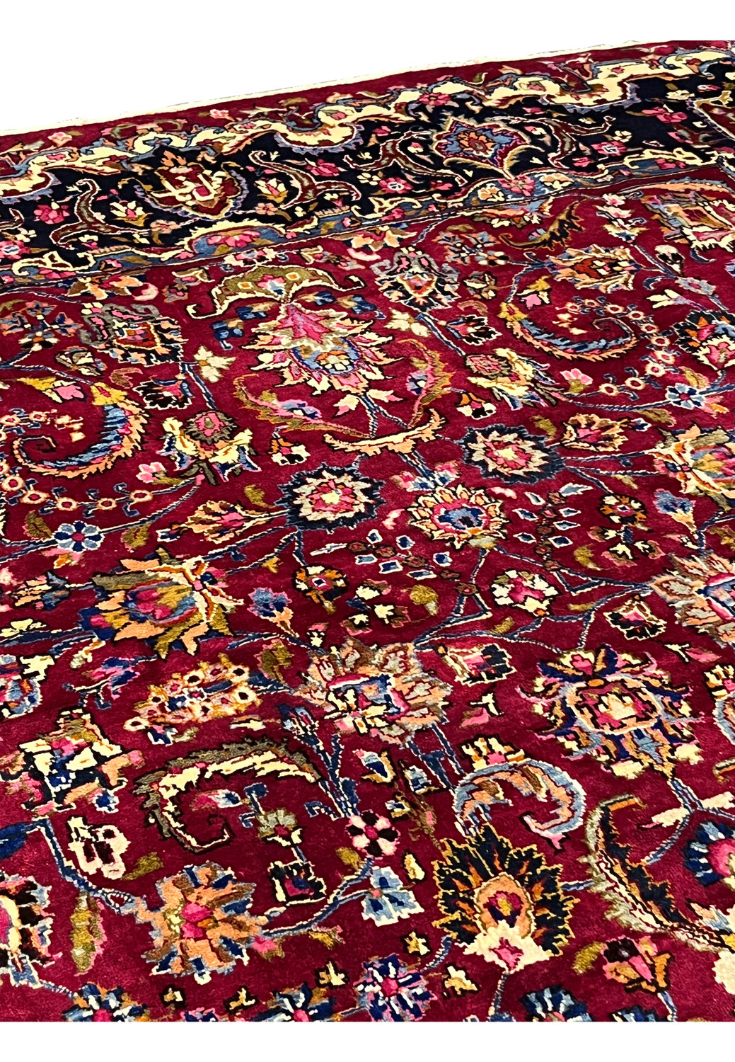 Design closeup of Persian Mashad rug showing symmetrical floral layout, brick red field, multicolor blossoms, and classic Persian composition.