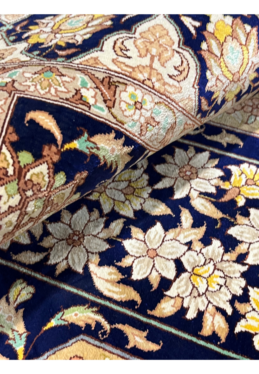 Angled rolled perspective revealing silk pile glow, layered borders and dense weave demonstrating luxury Persian Qum rug construction.