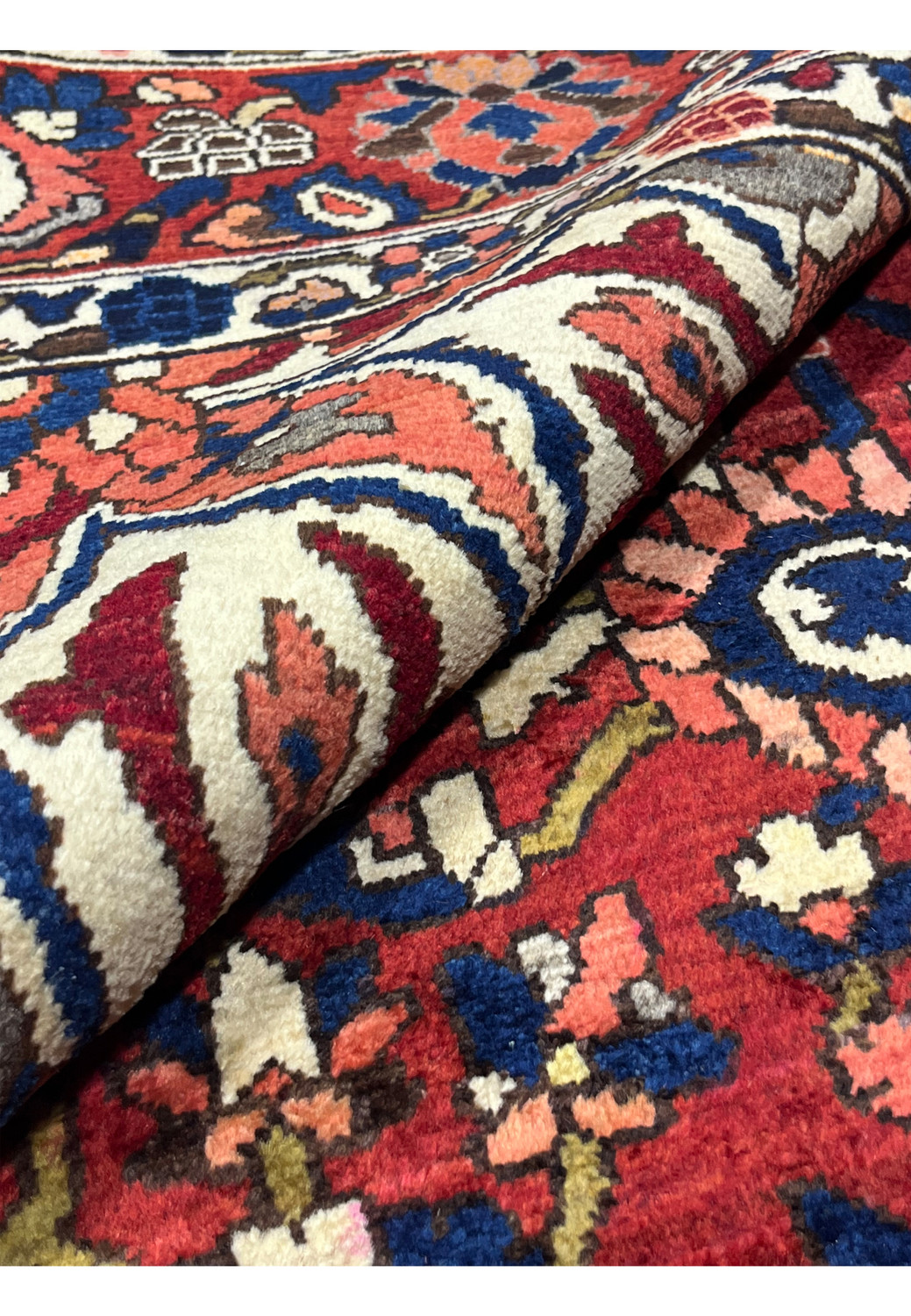 Rolled Persian Bakhtiari rug showing lush hand-knotted wool pile depth and vibrant red and blue colors.
