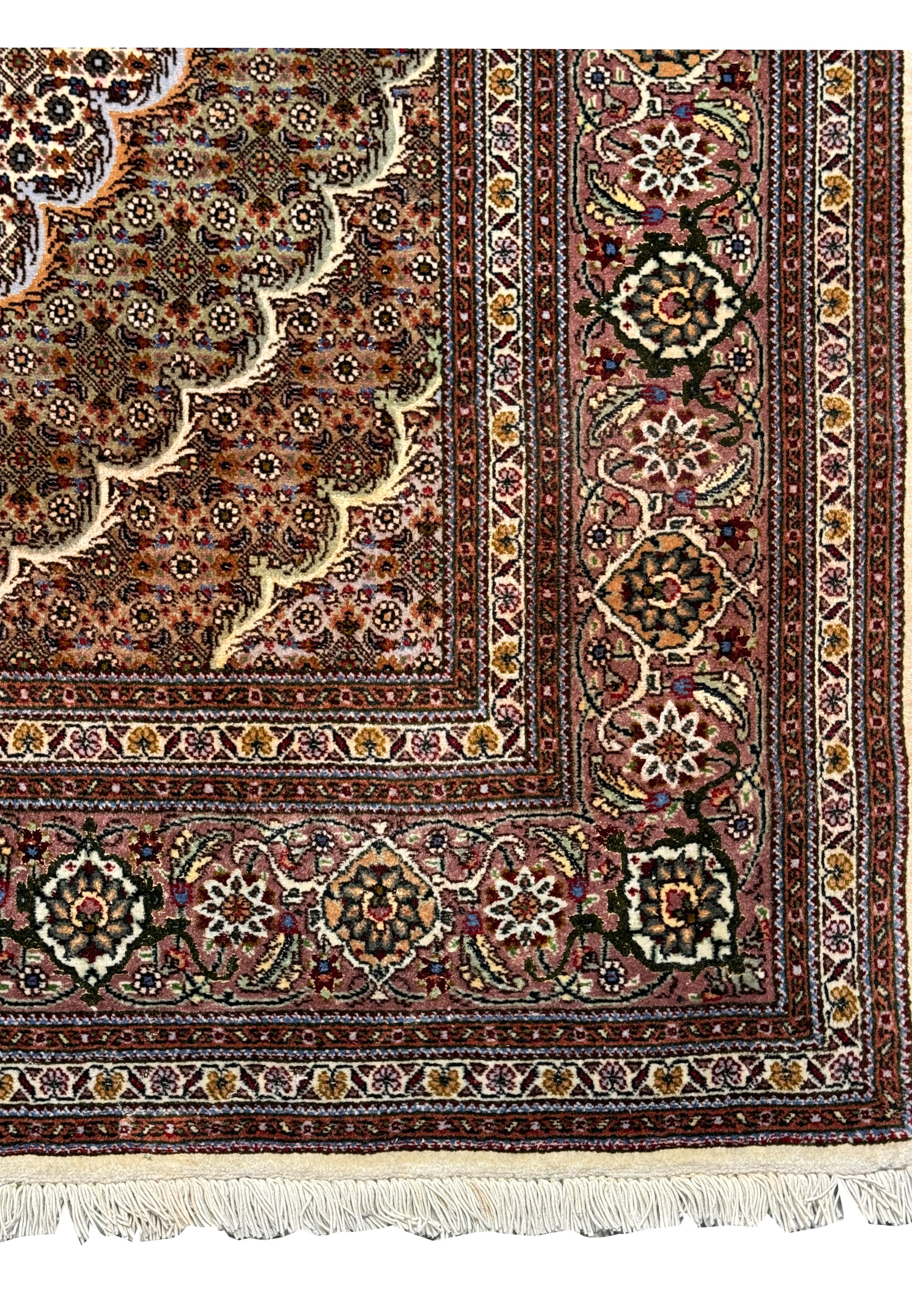 Close-up of the 5x7 Persian Tabriz Mahi rug's border, featuring detailed floral and geometric patterns in a variety of colors on a dark base, bordered by cream fringe.