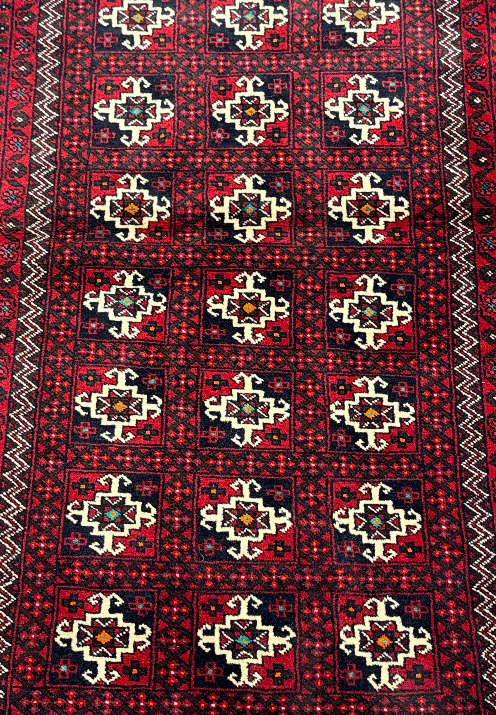 Close-up of a Persian Baluch rug showcasing detailed patterns with dark red, white, navy, and hints of green and orange