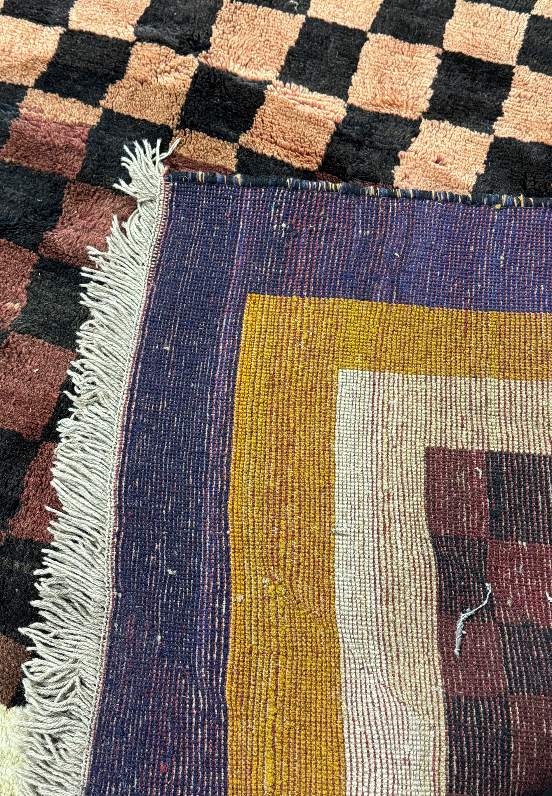 Detailed image of the corner of a modern Nepal rug, showing the fringe and the transition between the checkerboard center and the bold border colors.